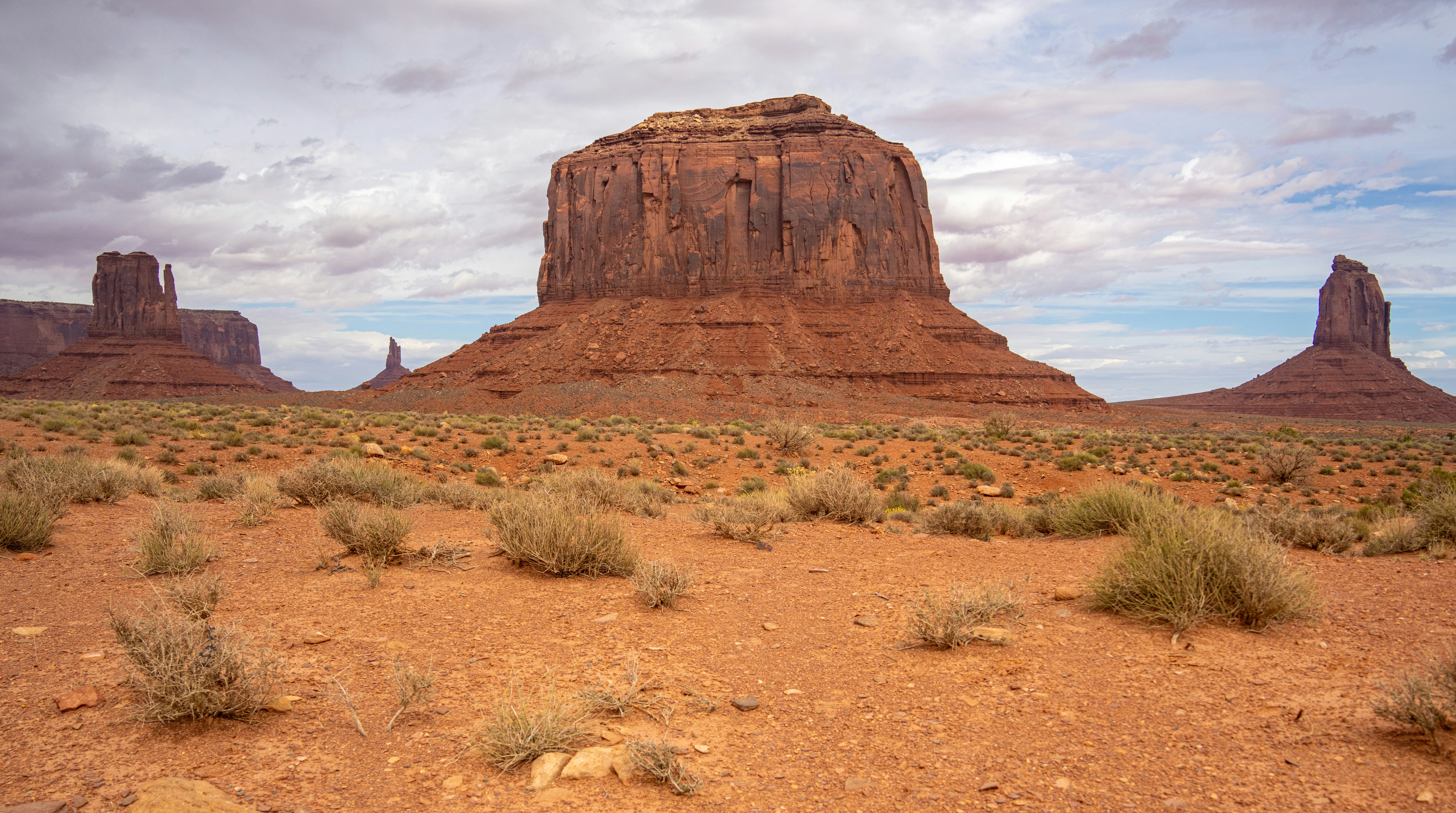 Butte di arenaria rossa che si innalzano dal suolo desertico sotto un cielo nuvoloso nella Monument Valley