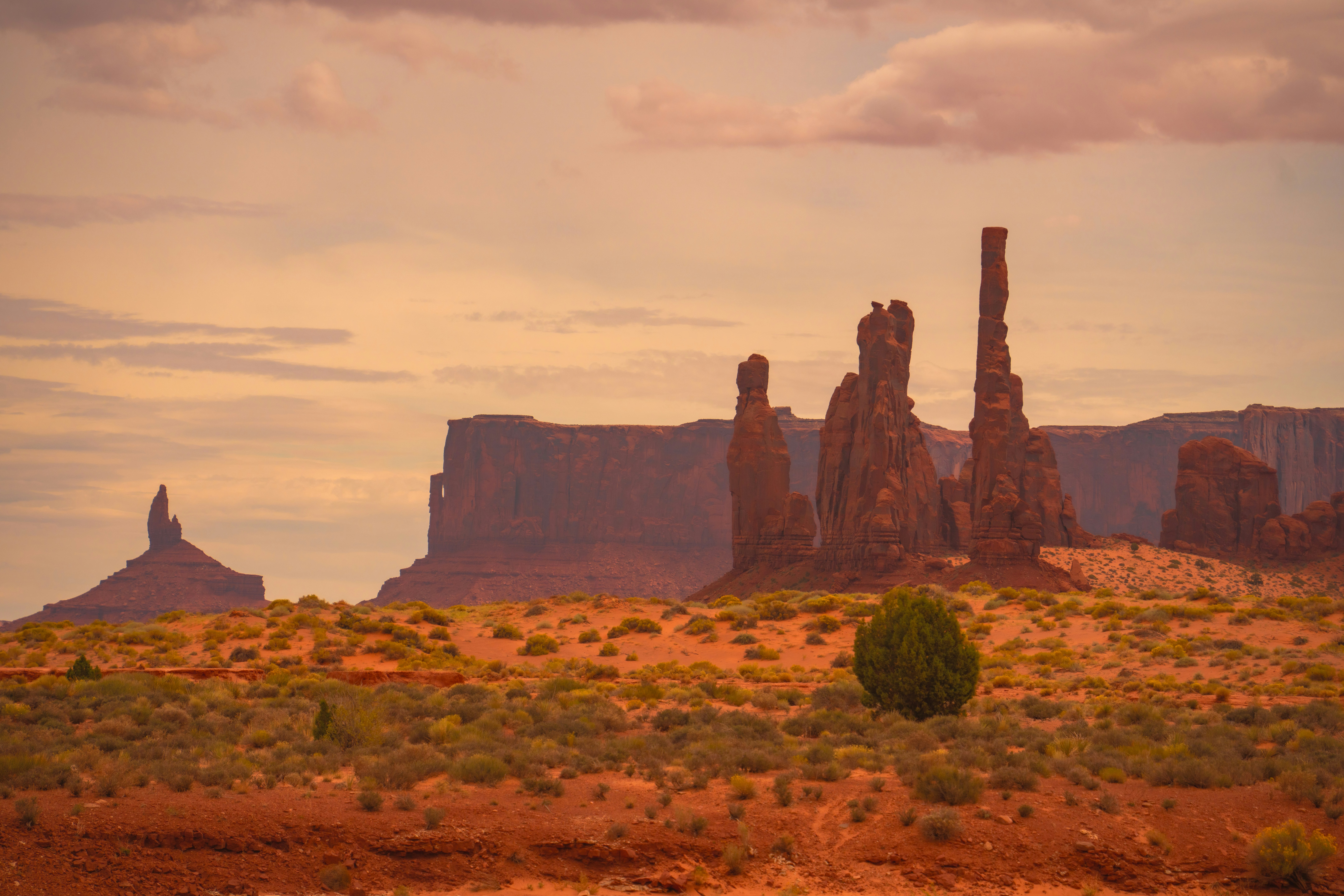 Red sandstone buttes and towering rock spires in Monument Valley under a warm orange sky