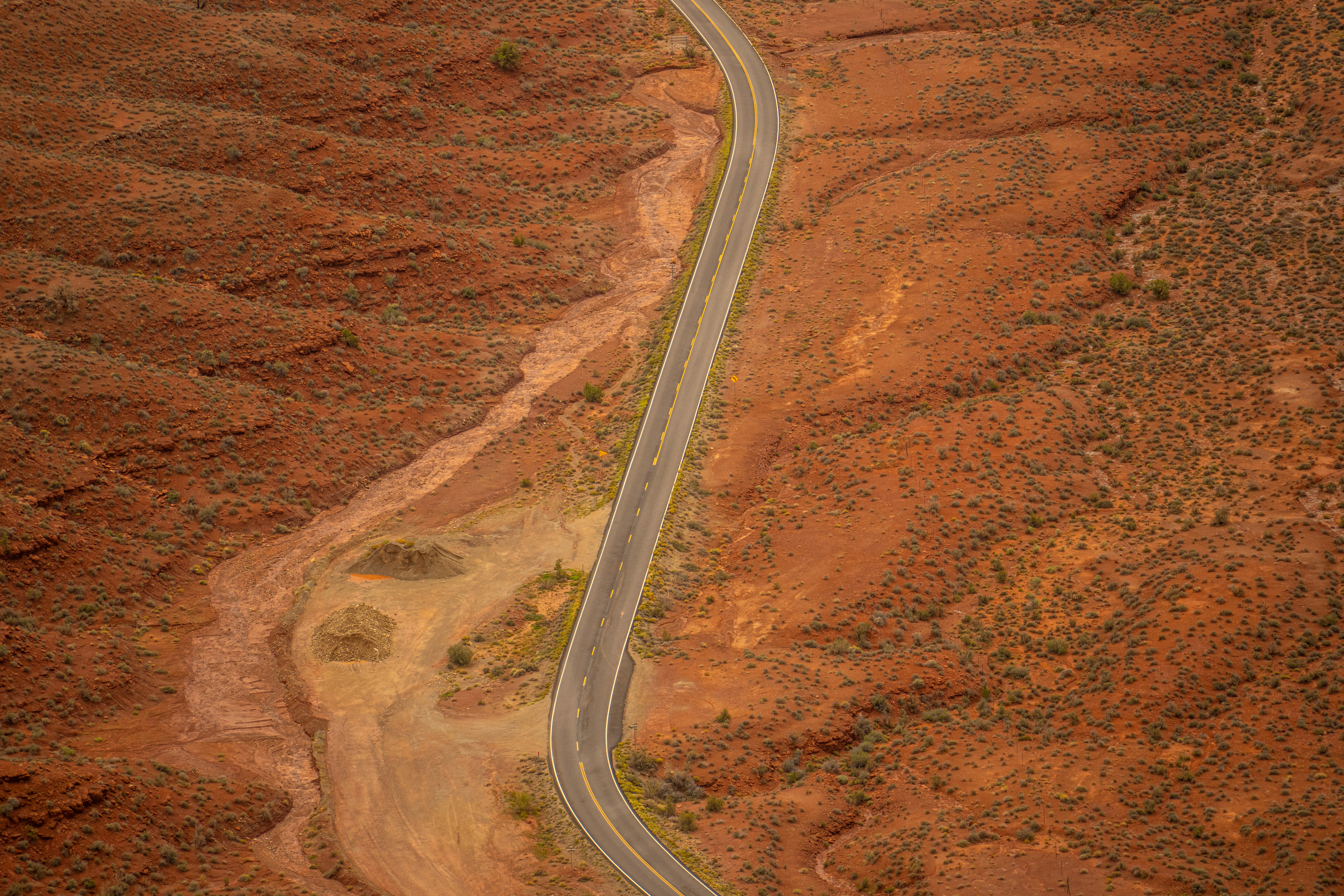 An aerial view of a winding road cutting through a vast red desert landscape