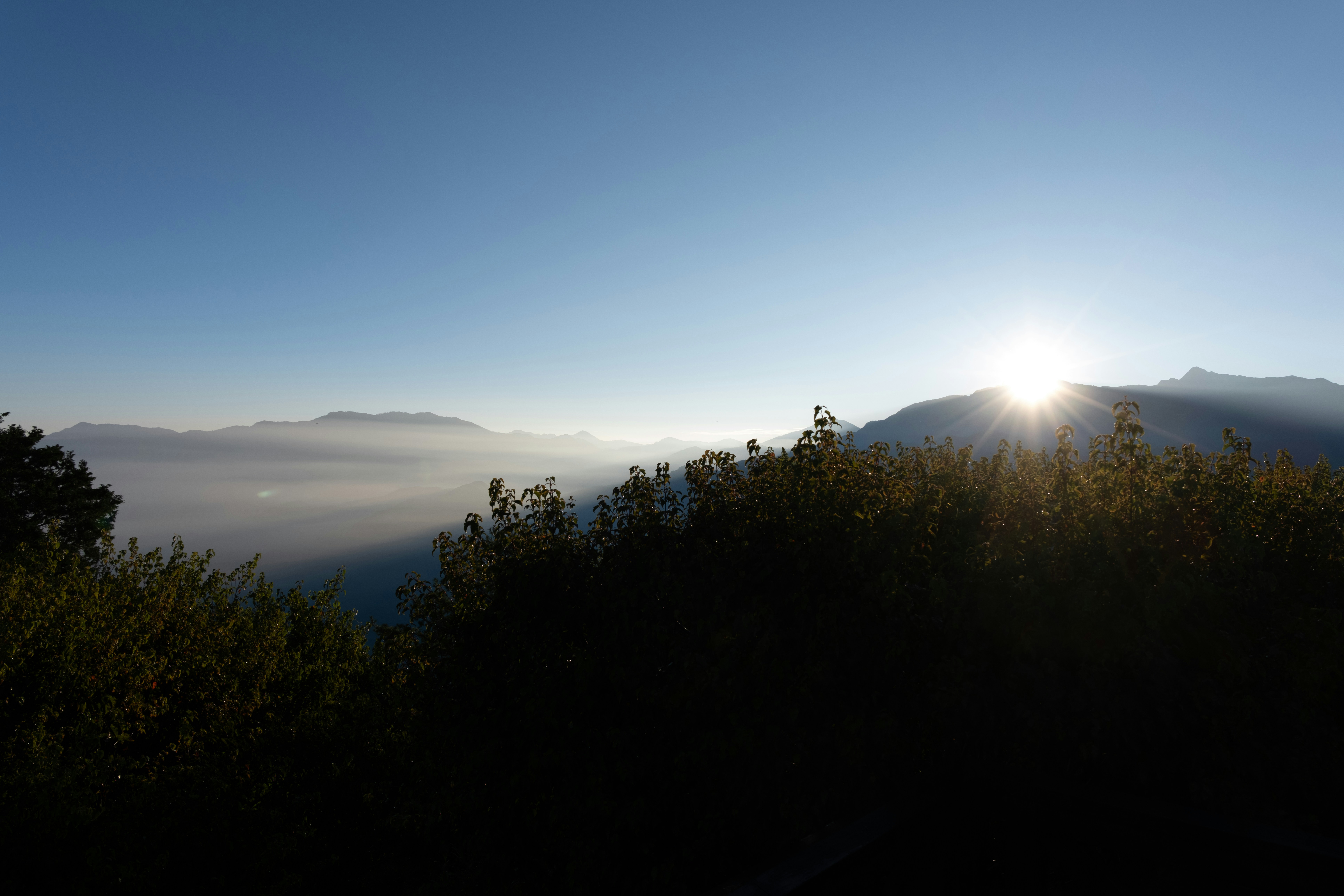 Sol bajo que se eleva sobre picos montañosos lejanos sobre un valle lleno de niebla matutina