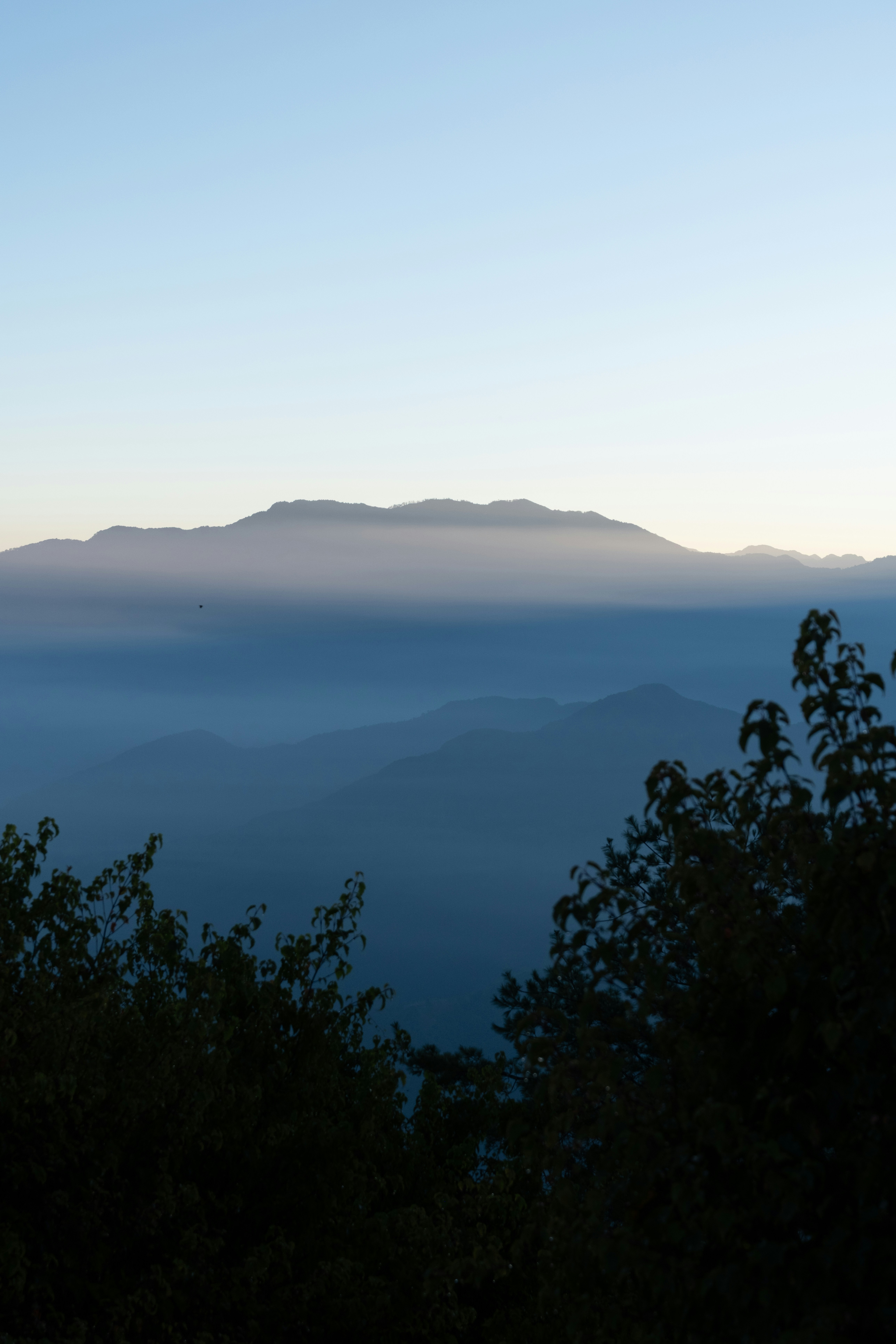 Crestas montañosas estratificadas que se desvanecen en niebla azul bajo un cielo pálido y claro