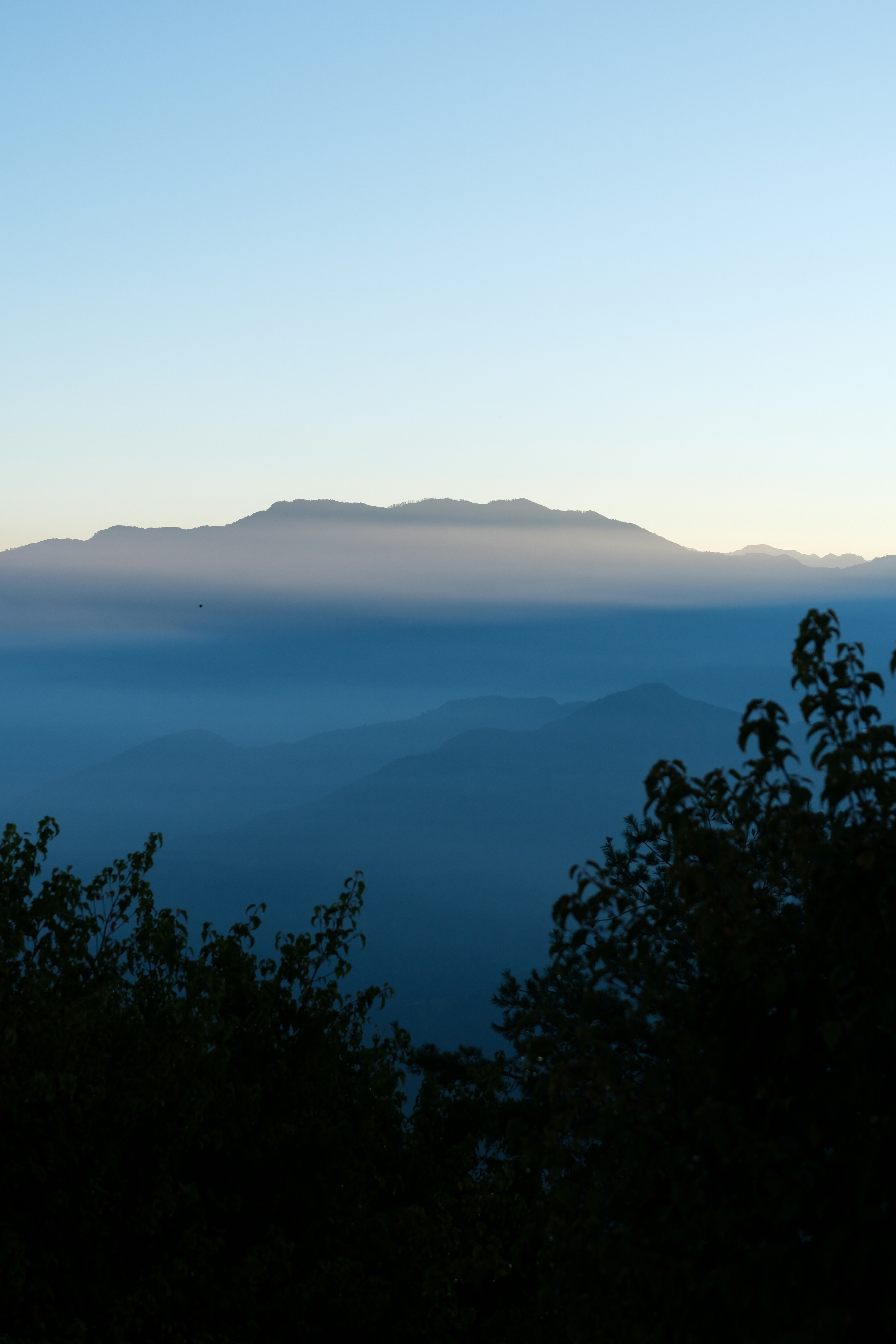 Crestas montañosas estratificadas que se desvanecen en niebla azul bajo un cielo pálido y claro