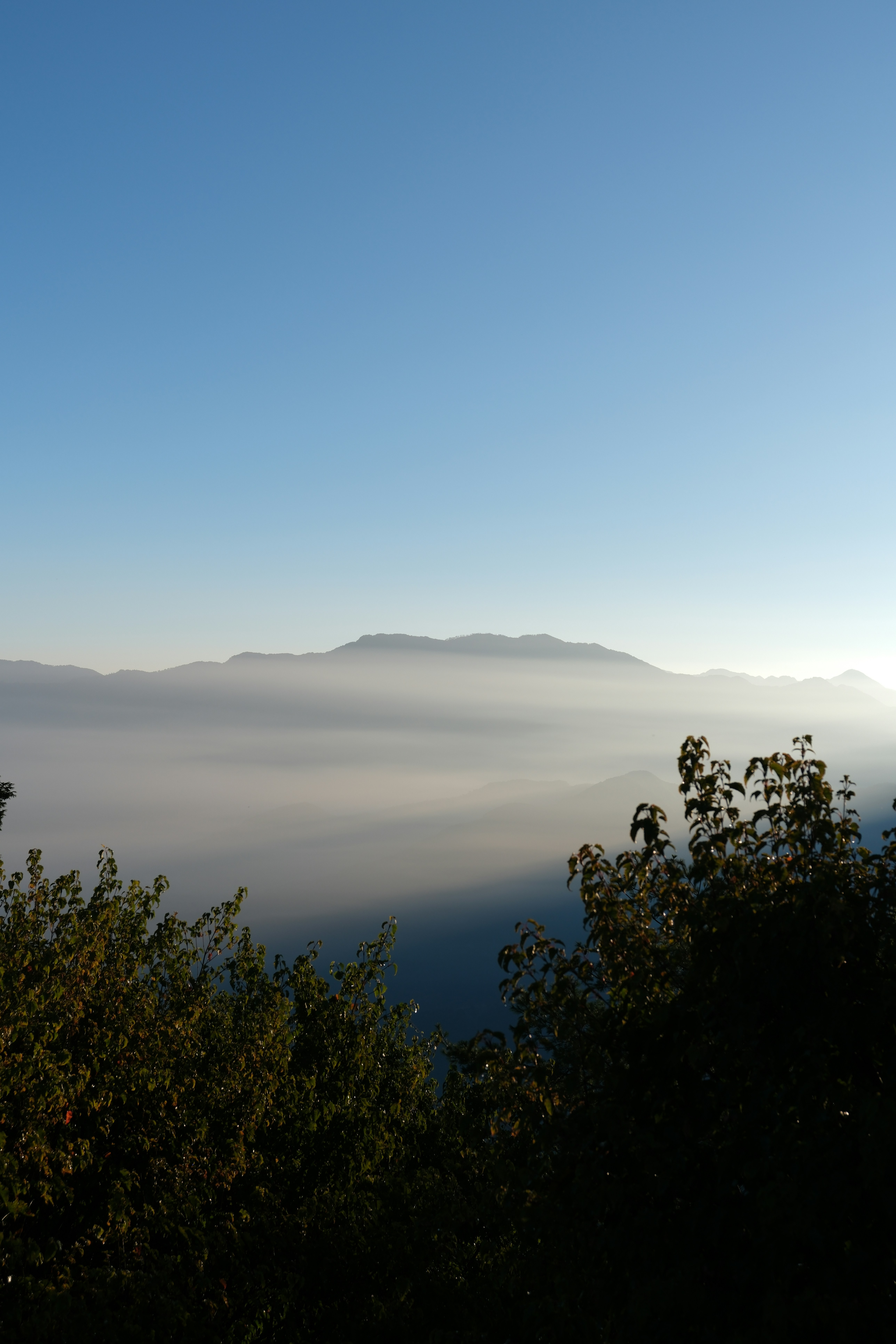 Montañas lejanas que se elevan sobre una densa capa de niebla de valle bajo un cielo azul claro