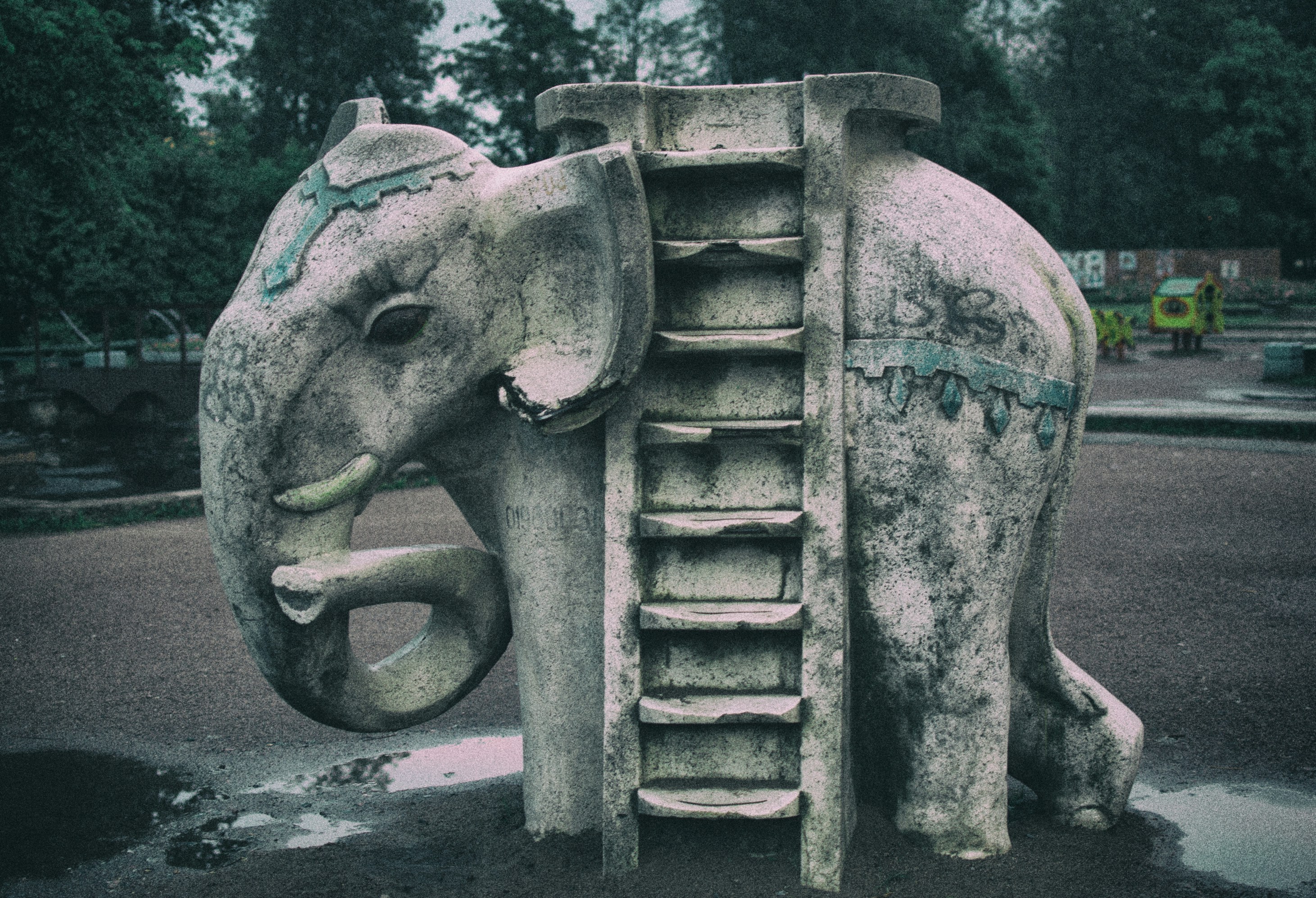 A weathered stone elephant sculpture with a built-in ladder in a park
