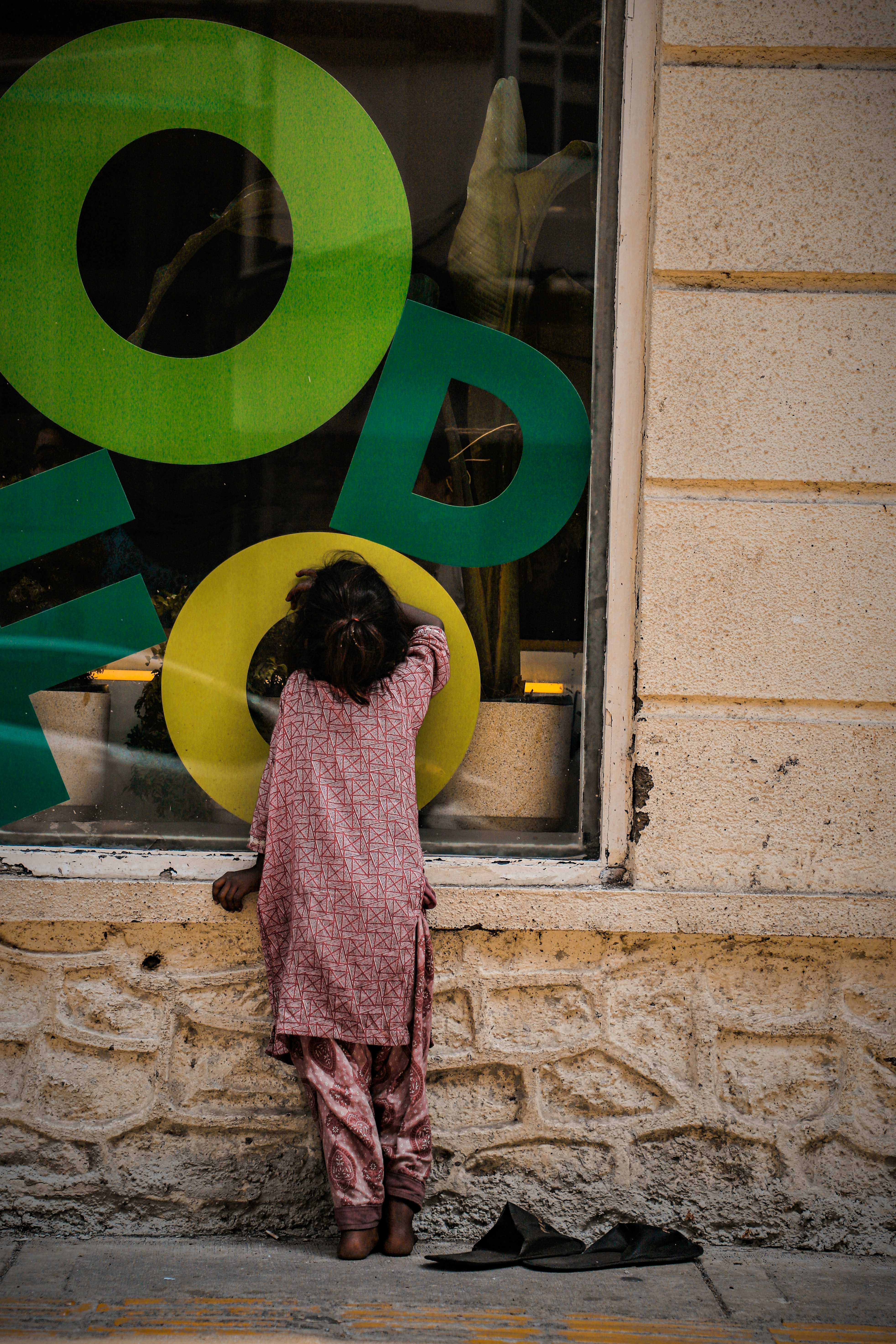 A child in a patterned tunic looking through a shop window with large green letters