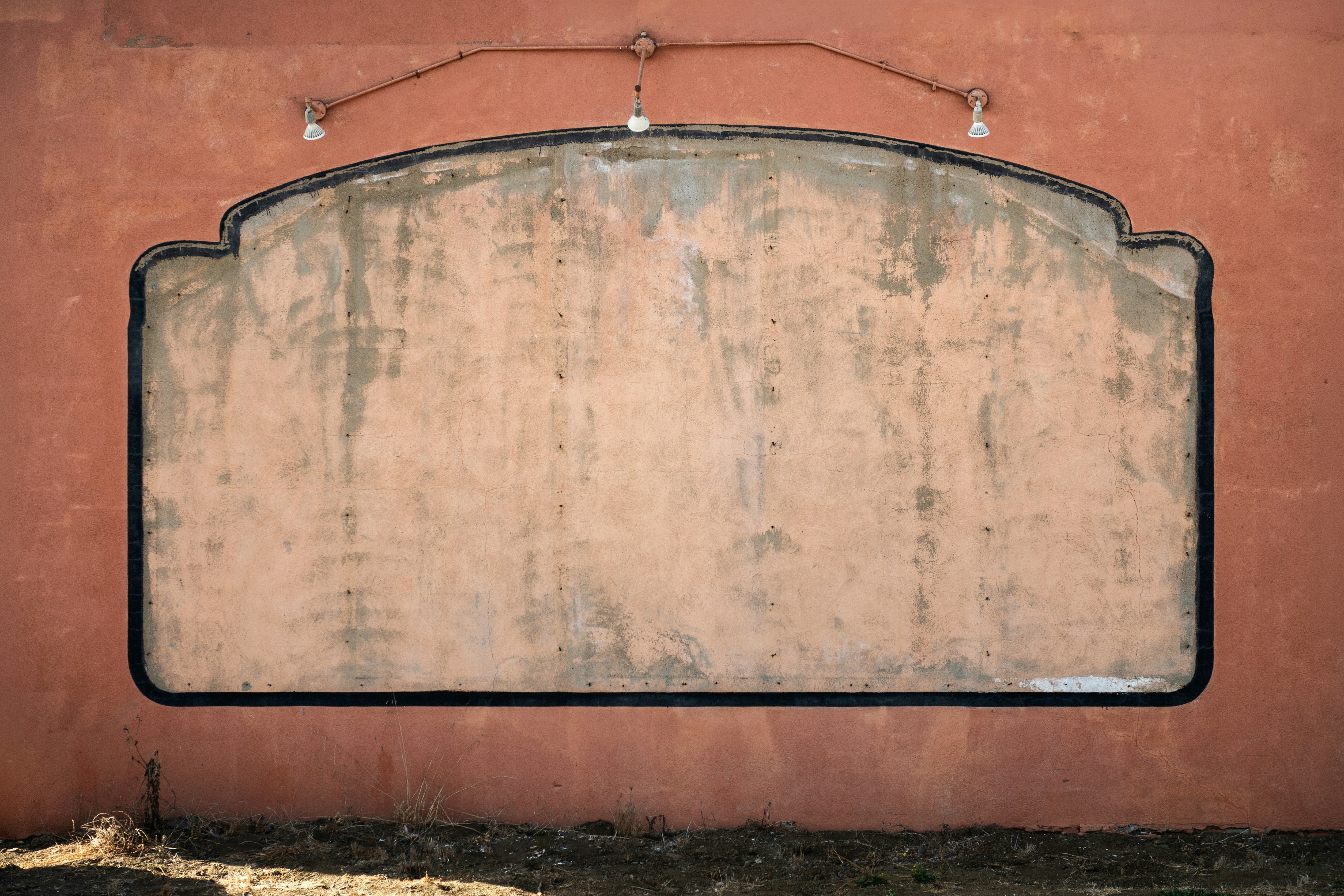 A weathered blank sign on a terracotta wall with three overhead lights