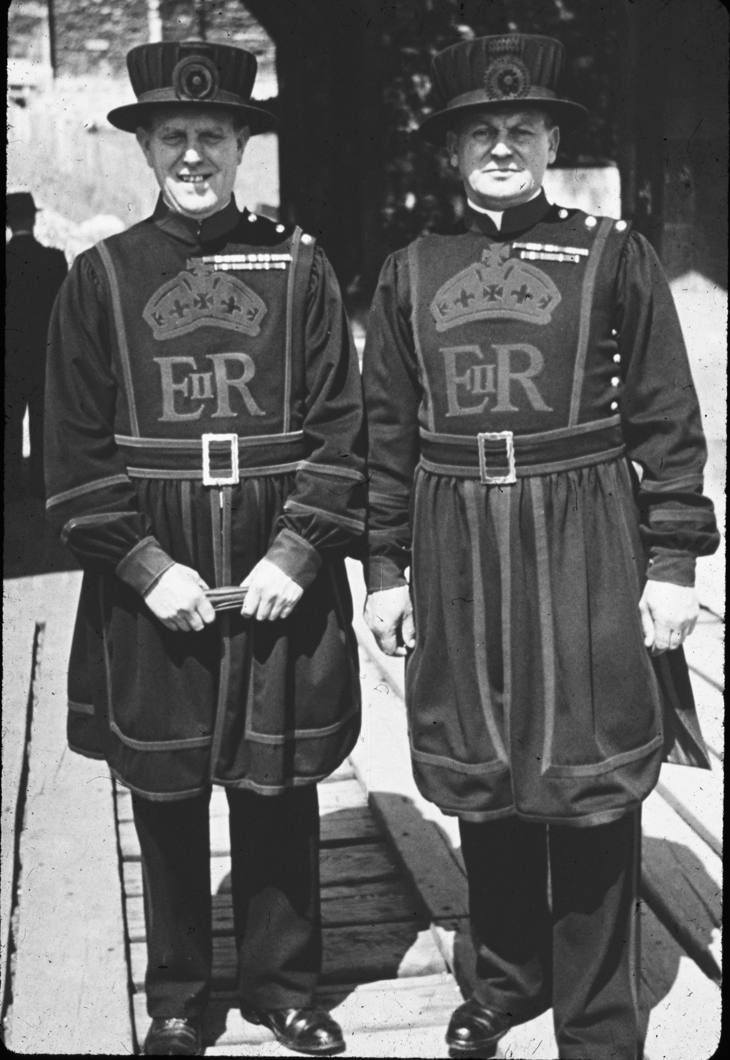 Two Yeoman Warders in traditional uniforms with ER insignia standing on a wooden walkway