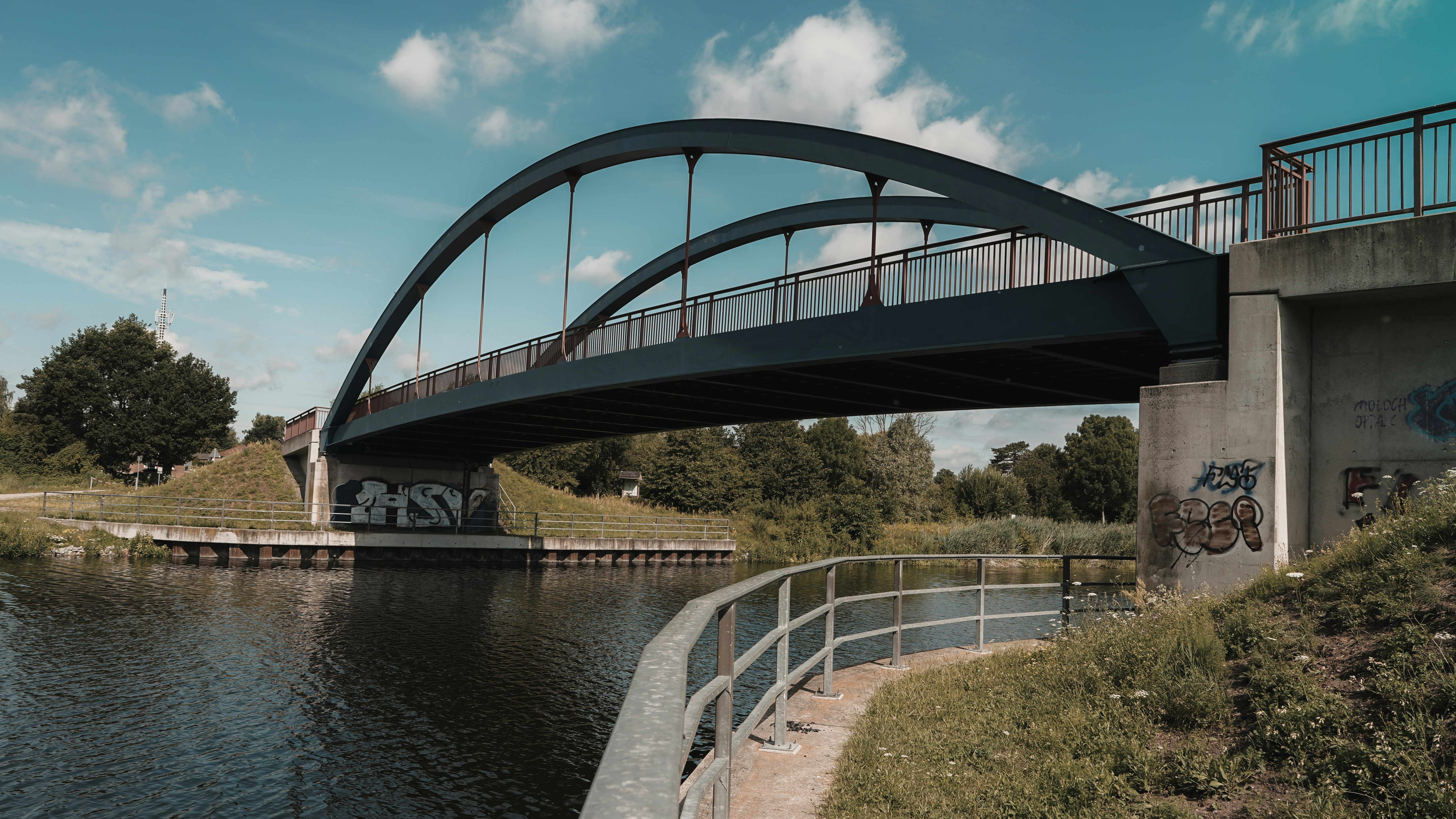 A dark blue arched bridge over a calm river with graffiti on the concrete supports