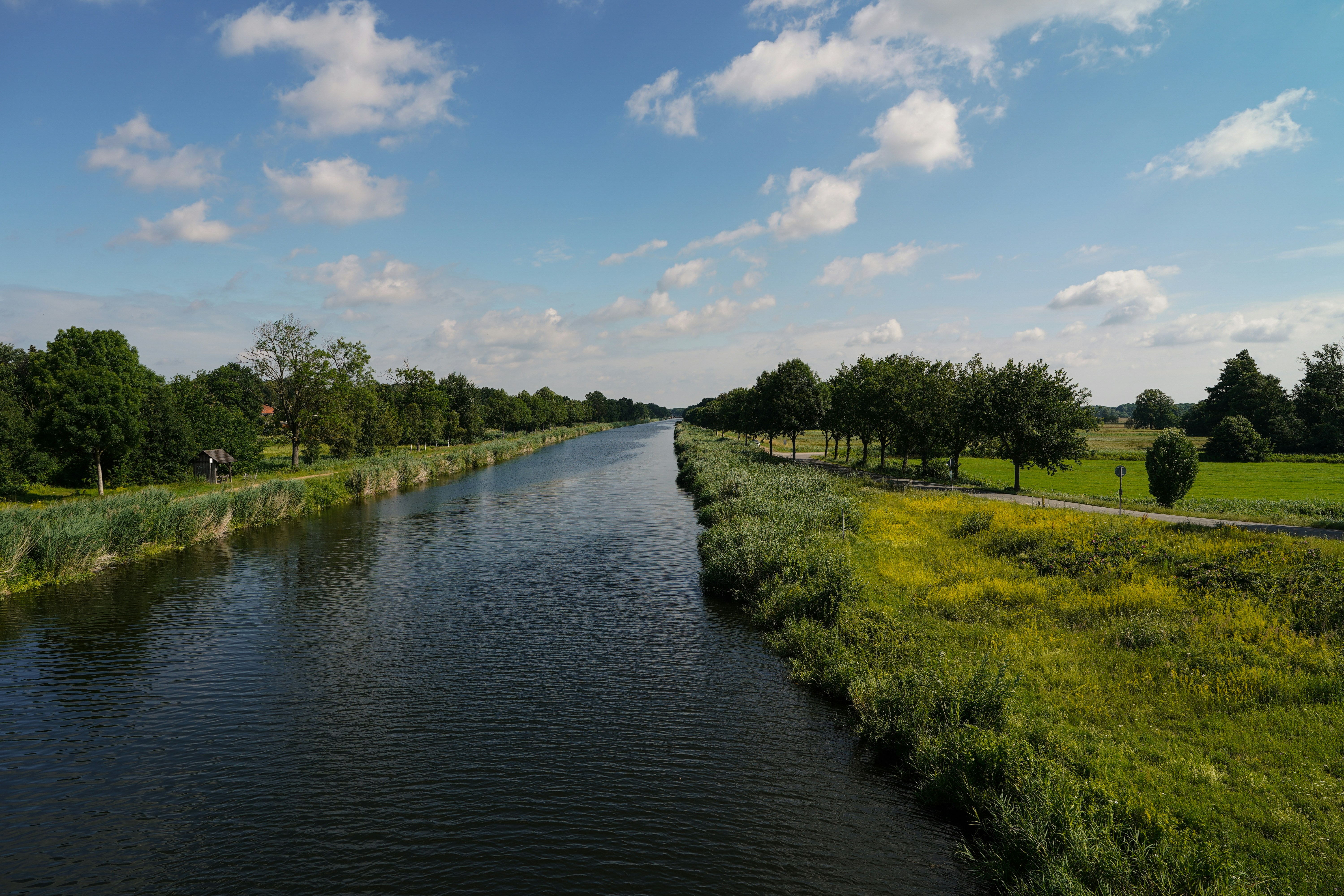 A calm canal flowing through a green landscape with trees and a blue sky