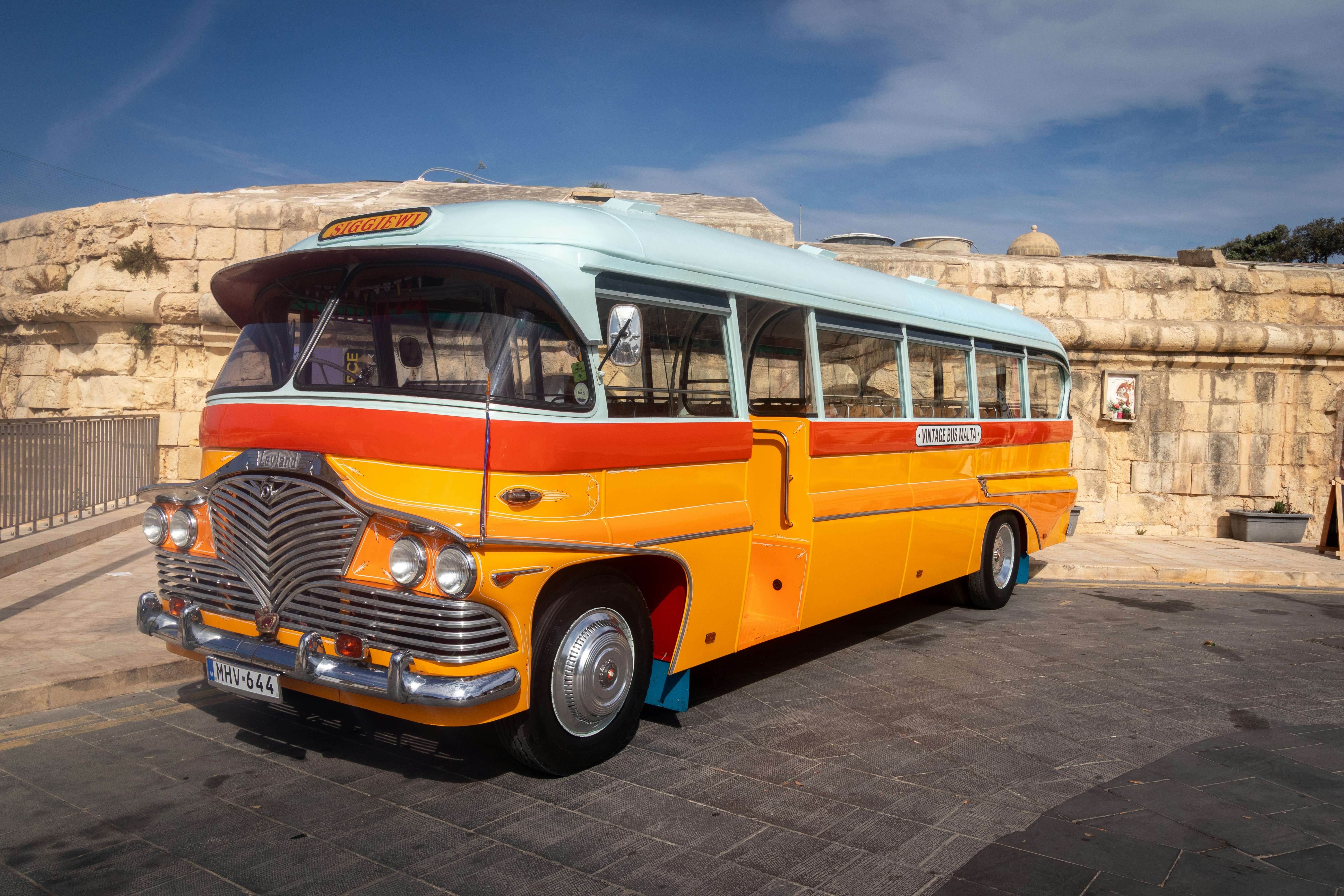 Ein vintage gelb-oranger Bus parkte vor einer Steinmauer auf Malta