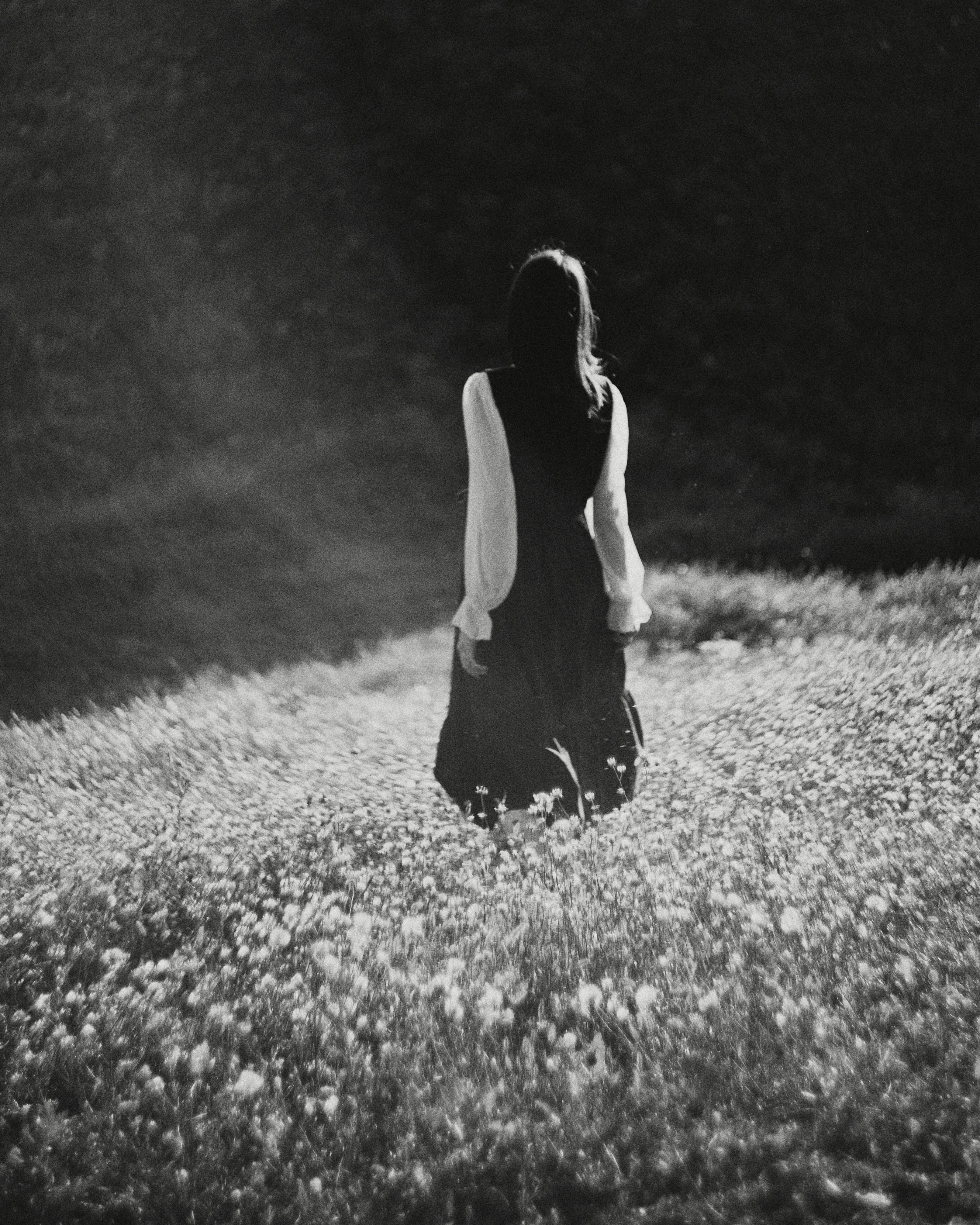A woman in a long dress walking through a field of wildflowers at night