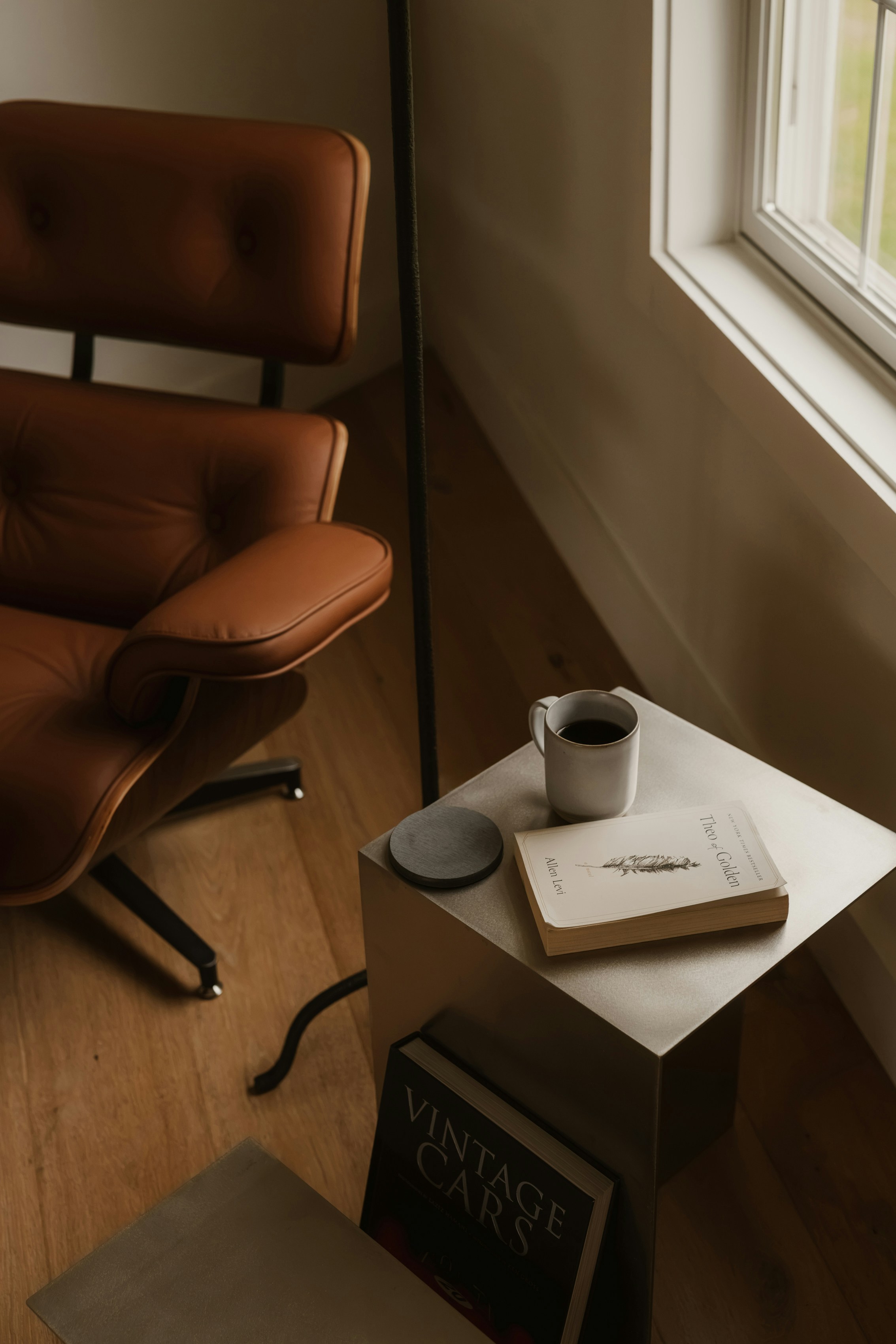 A brown leather lounge chair beside a metal side table with a book and coffee mug