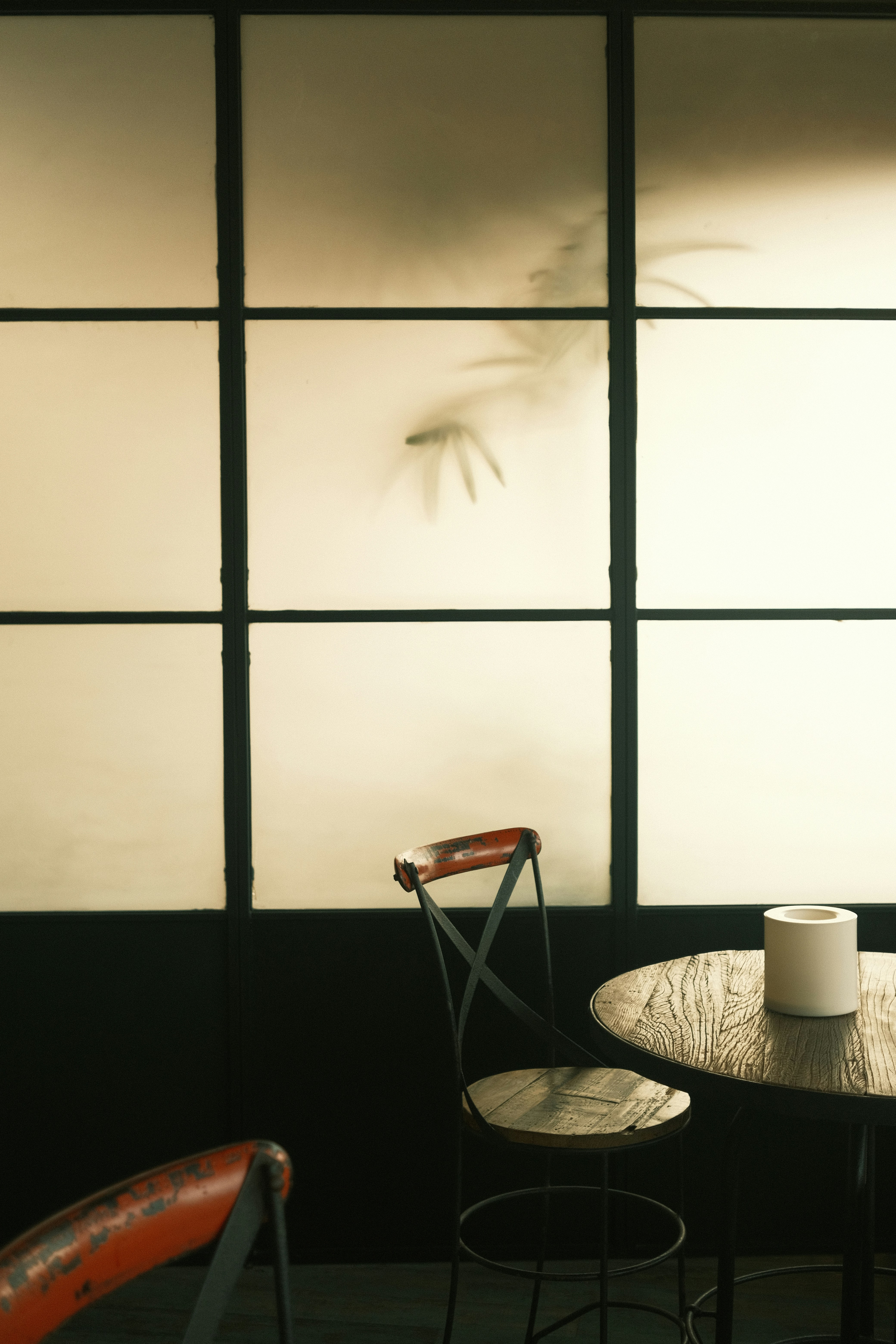 A wooden table and a metal chair in front of a frosted glass window with bamboo shadows
