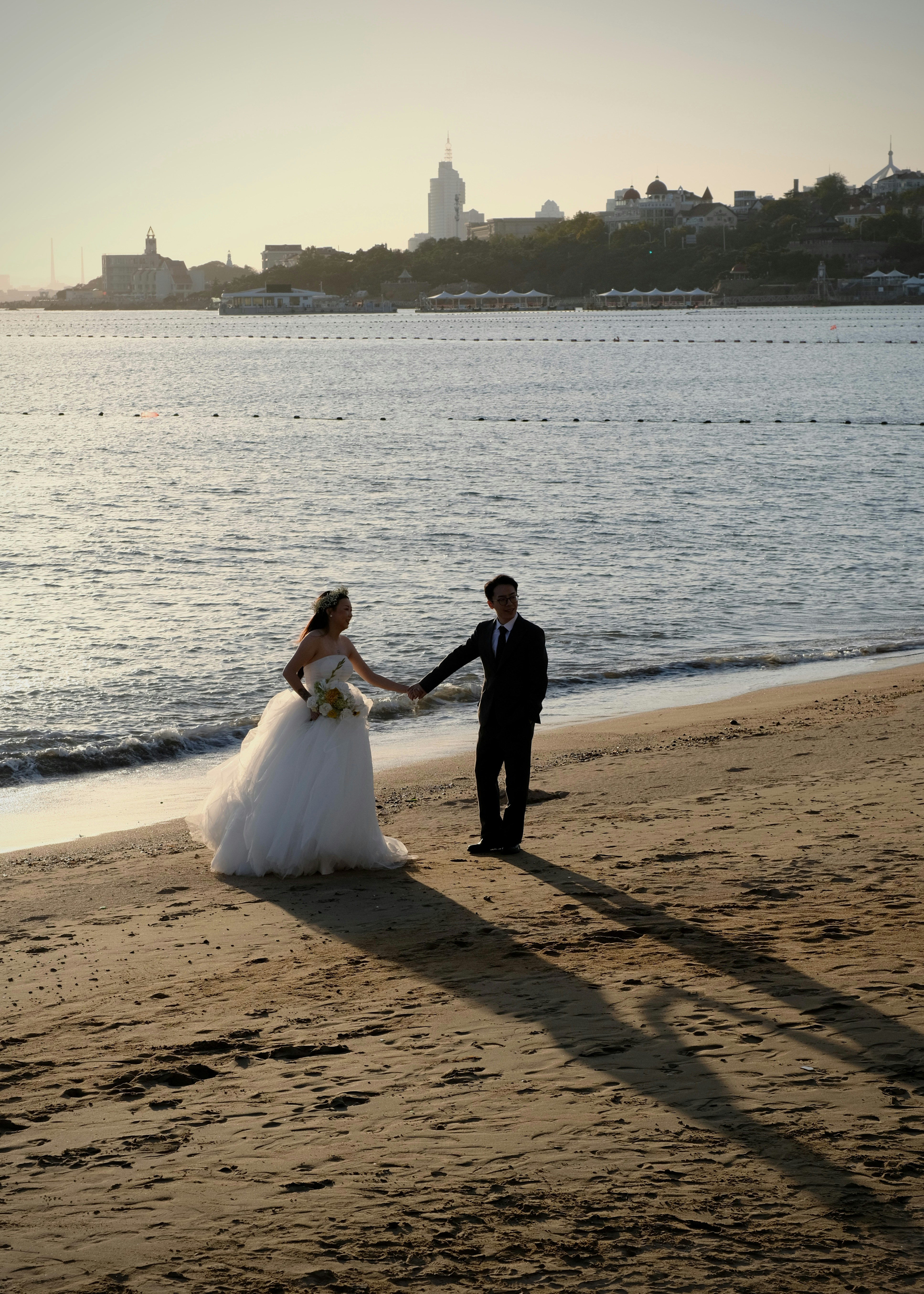 A bride and groom holding hands on a sandy beach at low sun