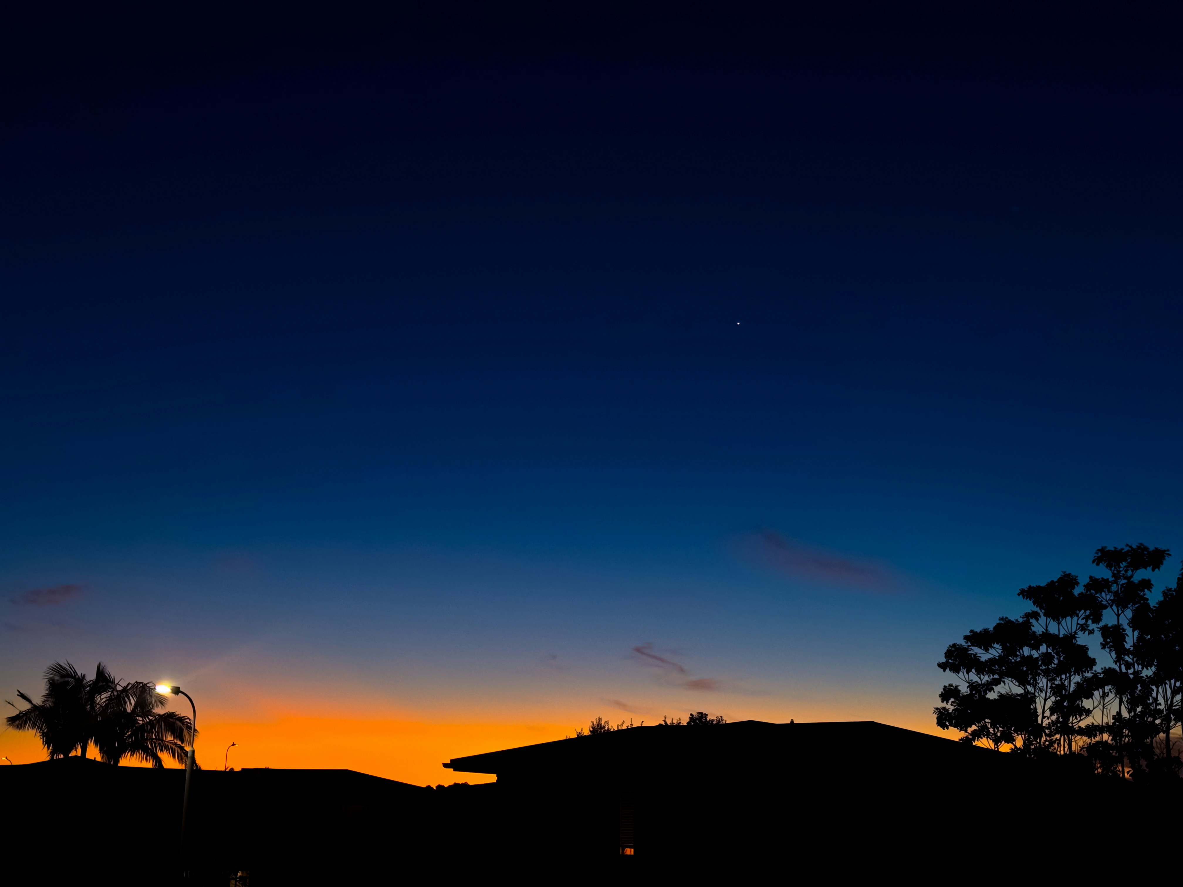 Silhouetted rooftops and trees against a vibrant orange and deep blue sky