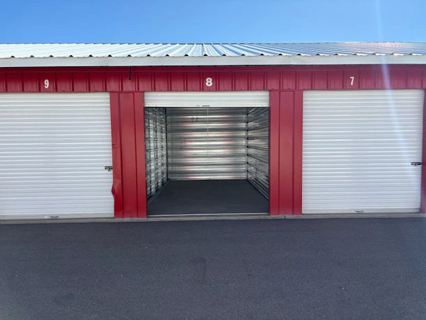 An open storage unit door numbered eight between two closed units under a metal roof