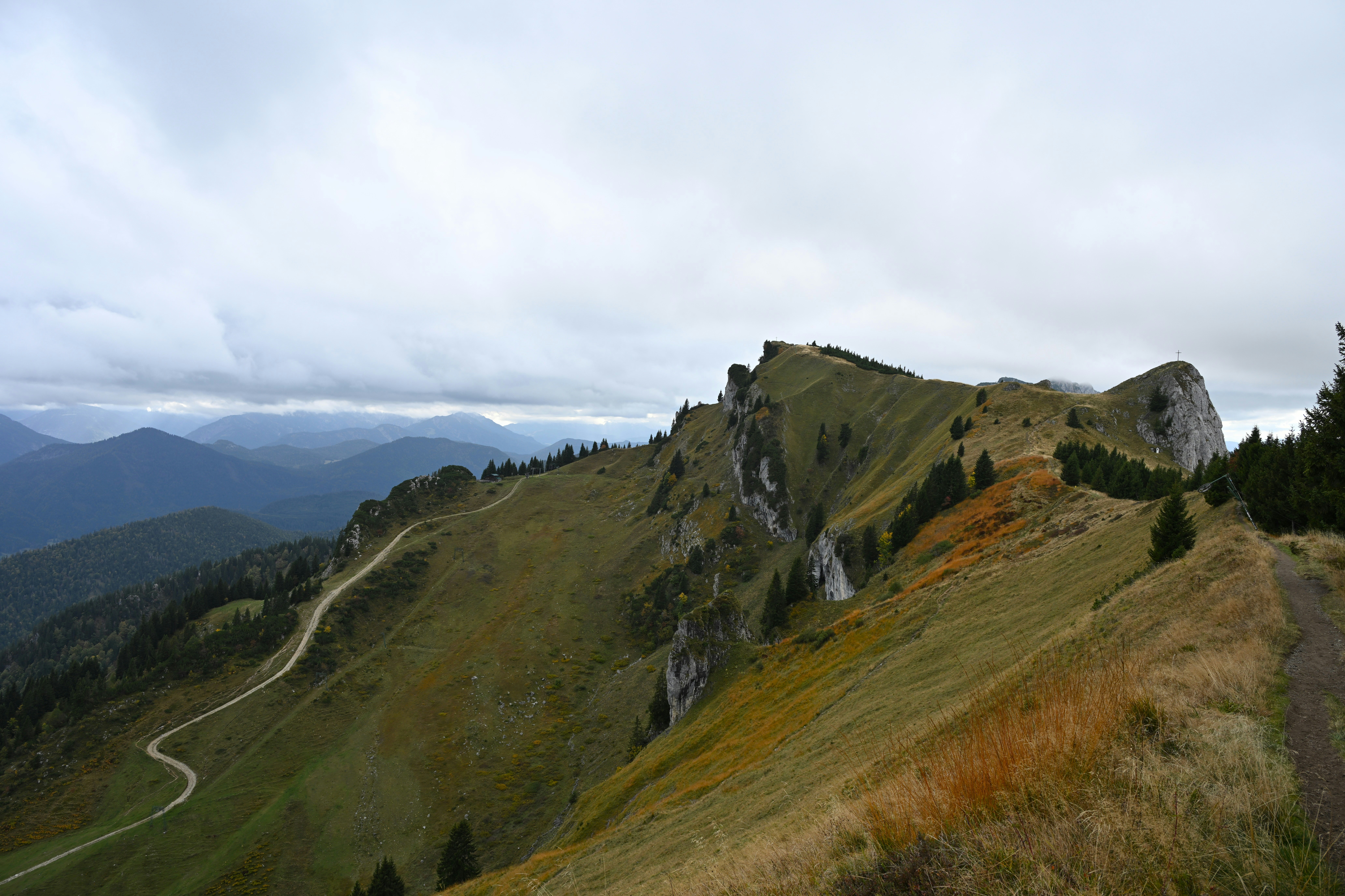A winding dirt path along a grassy mountain ridge under a cloudy sky