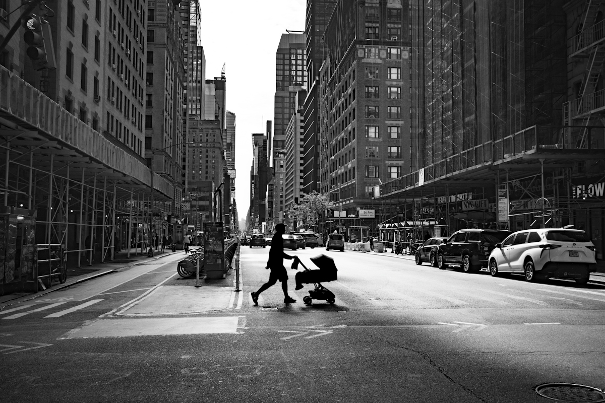 A person in silhouette pushing a stroller across a wide city street in New York