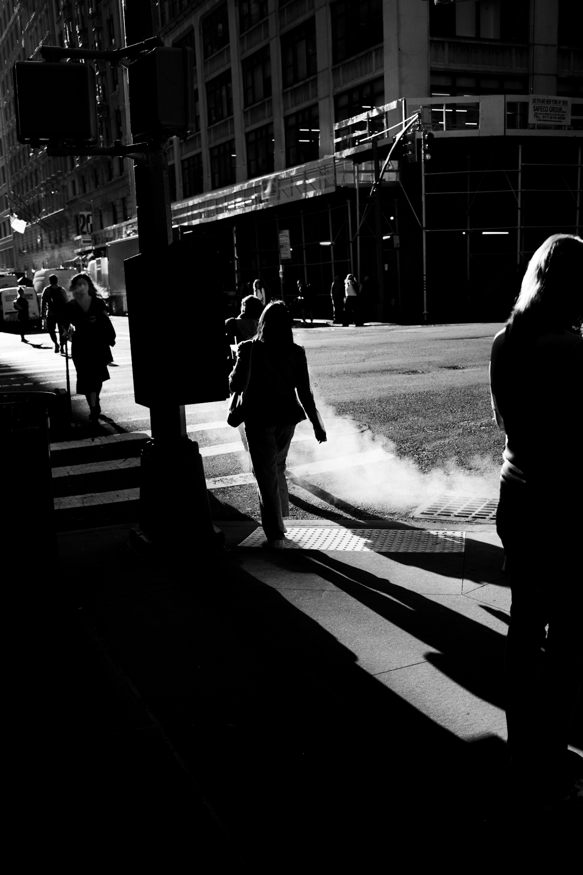 People crossing a city street with steam rising from a manhole cover in high contrast black and white