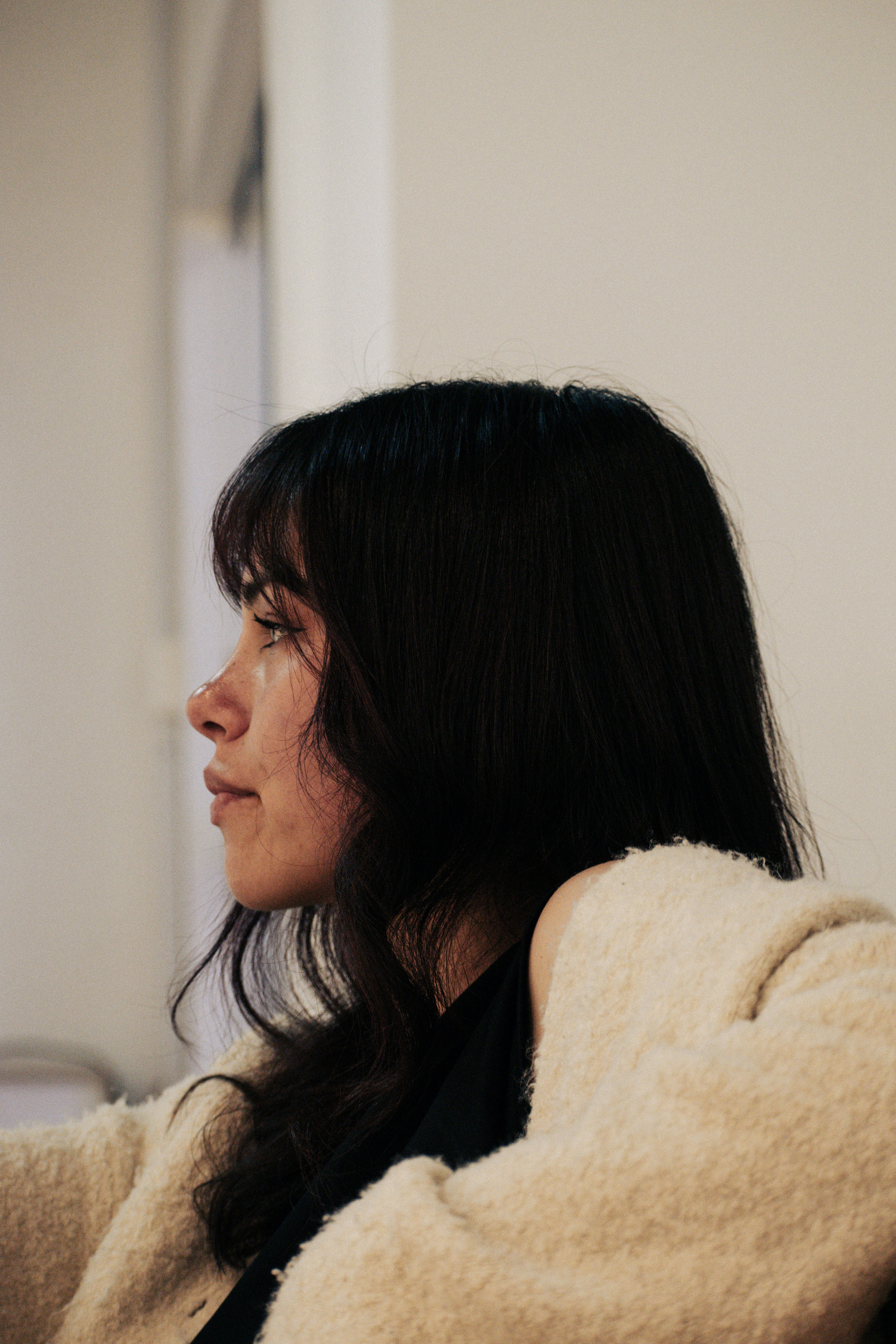 Uma mulher de cabelo escuro e franja de perfil usando um cardigã de textura bege