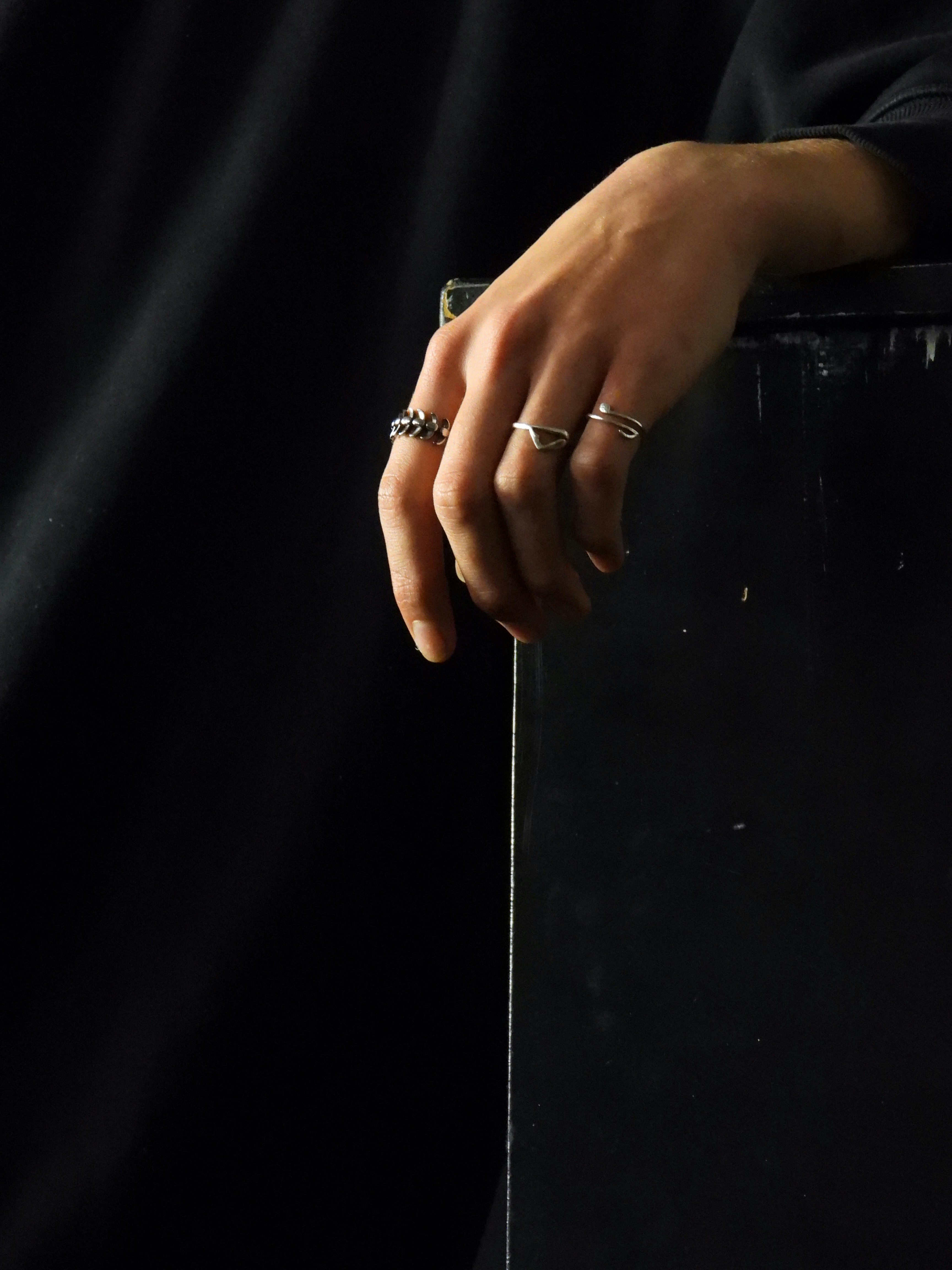 A hand with three silver rings resting on the edge of a black surface