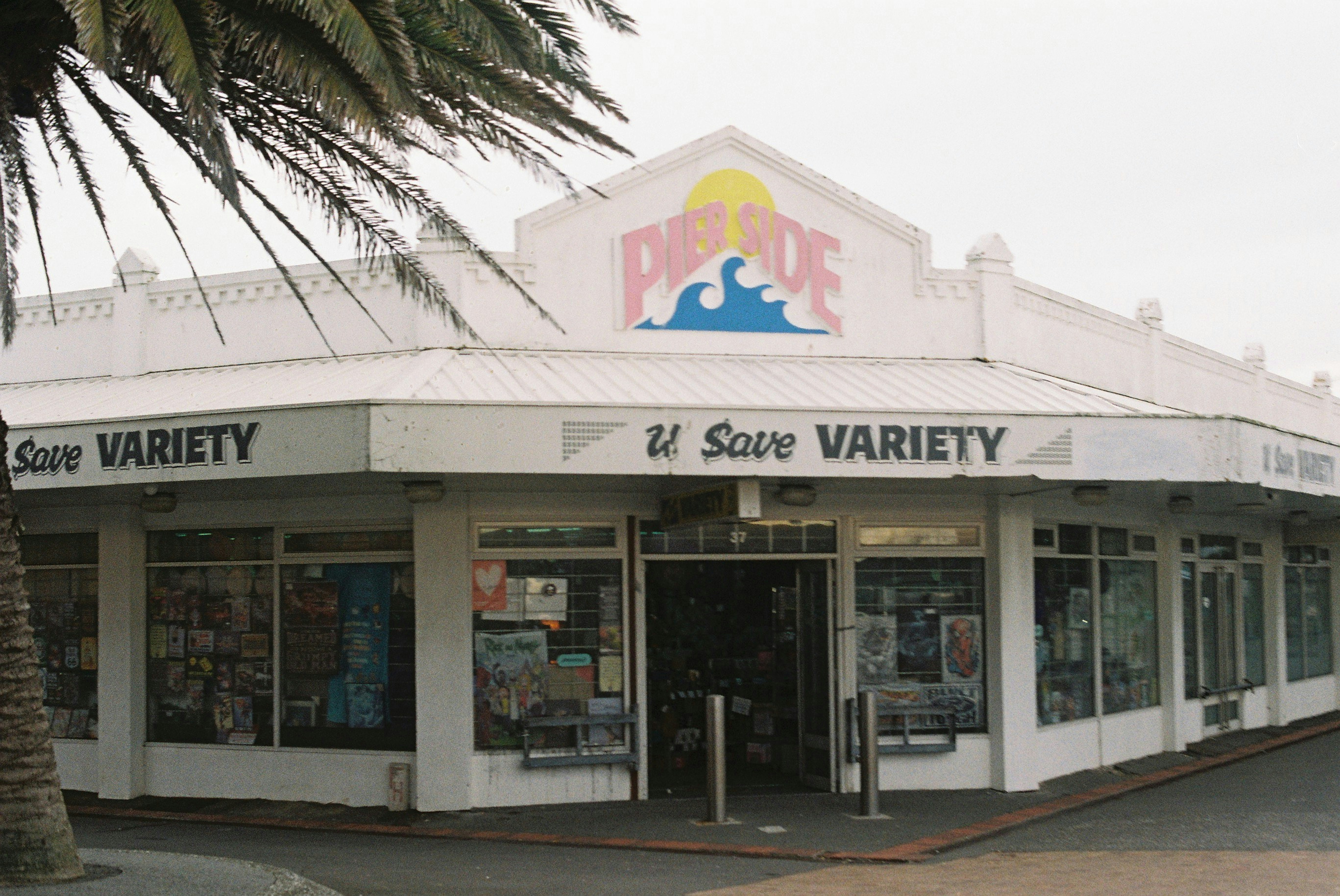 The Pier Side U Save Variety store with large windows and a palm tree in the foreground