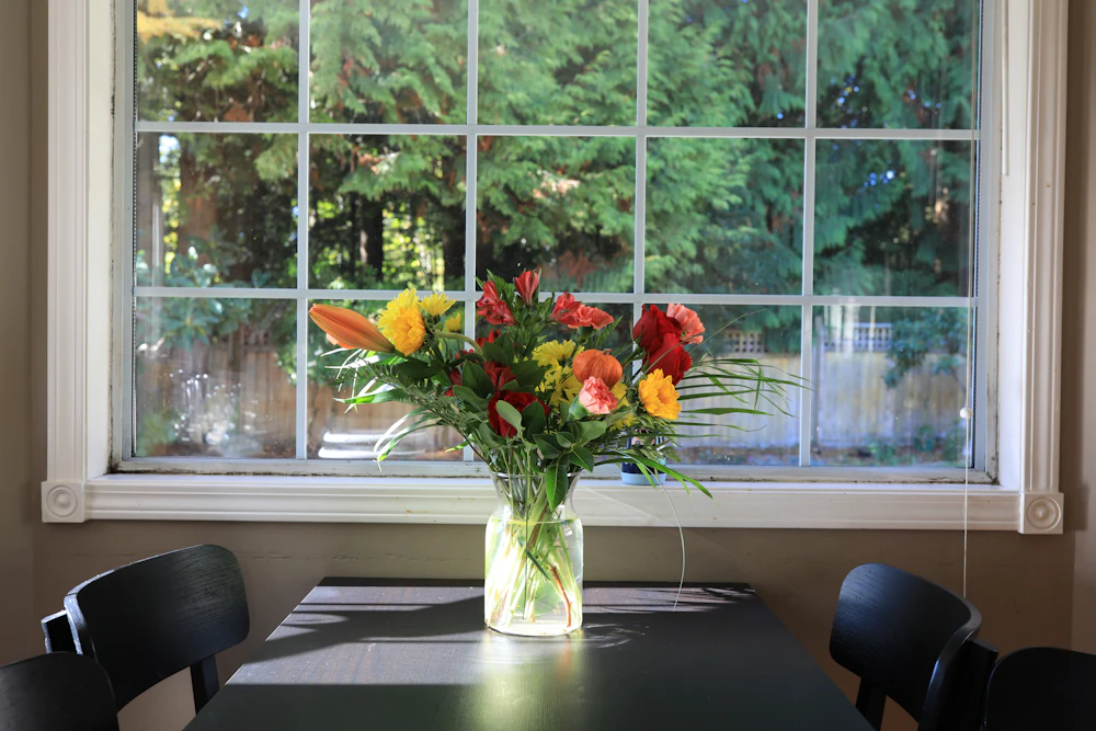 Glass vase of colourful flowers in front of a window