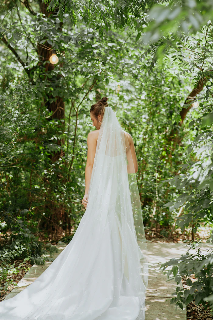 Bride with a long veil on a stone path in the forest