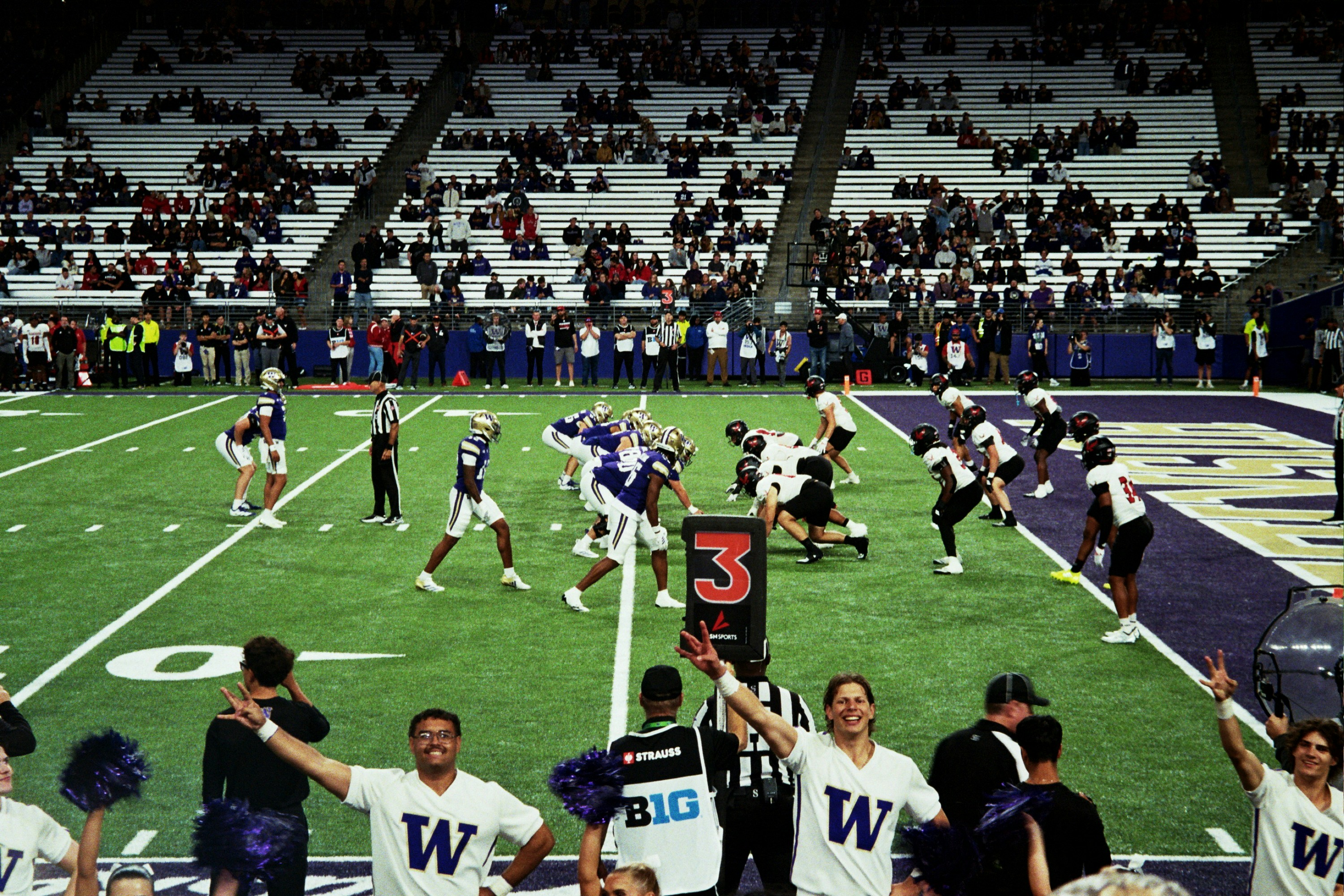 Cheerleaders in white jerseys with a W logo cheering in front of a football game