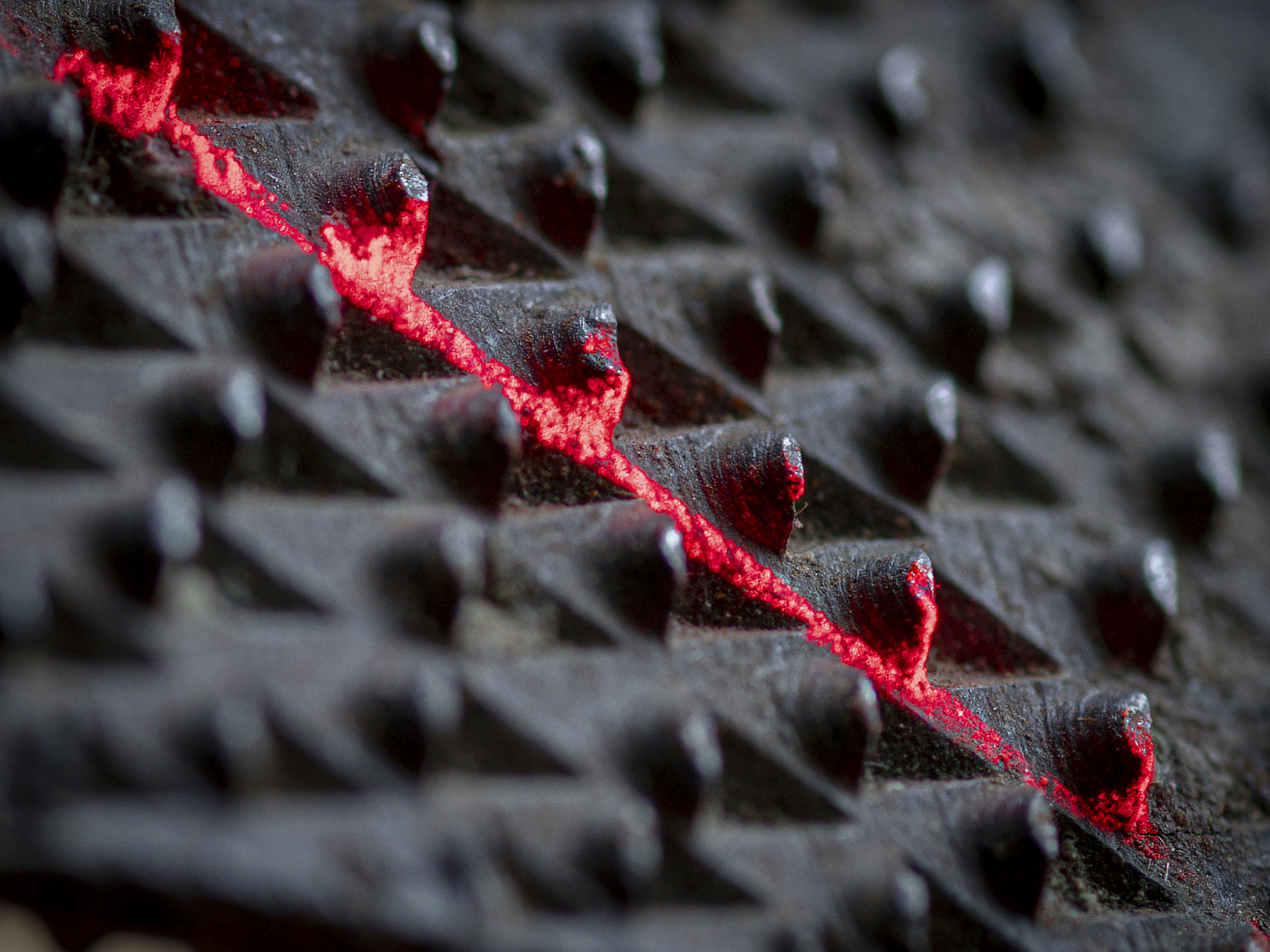 A dark textured metal surface with a jagged crack glowing with bright red light