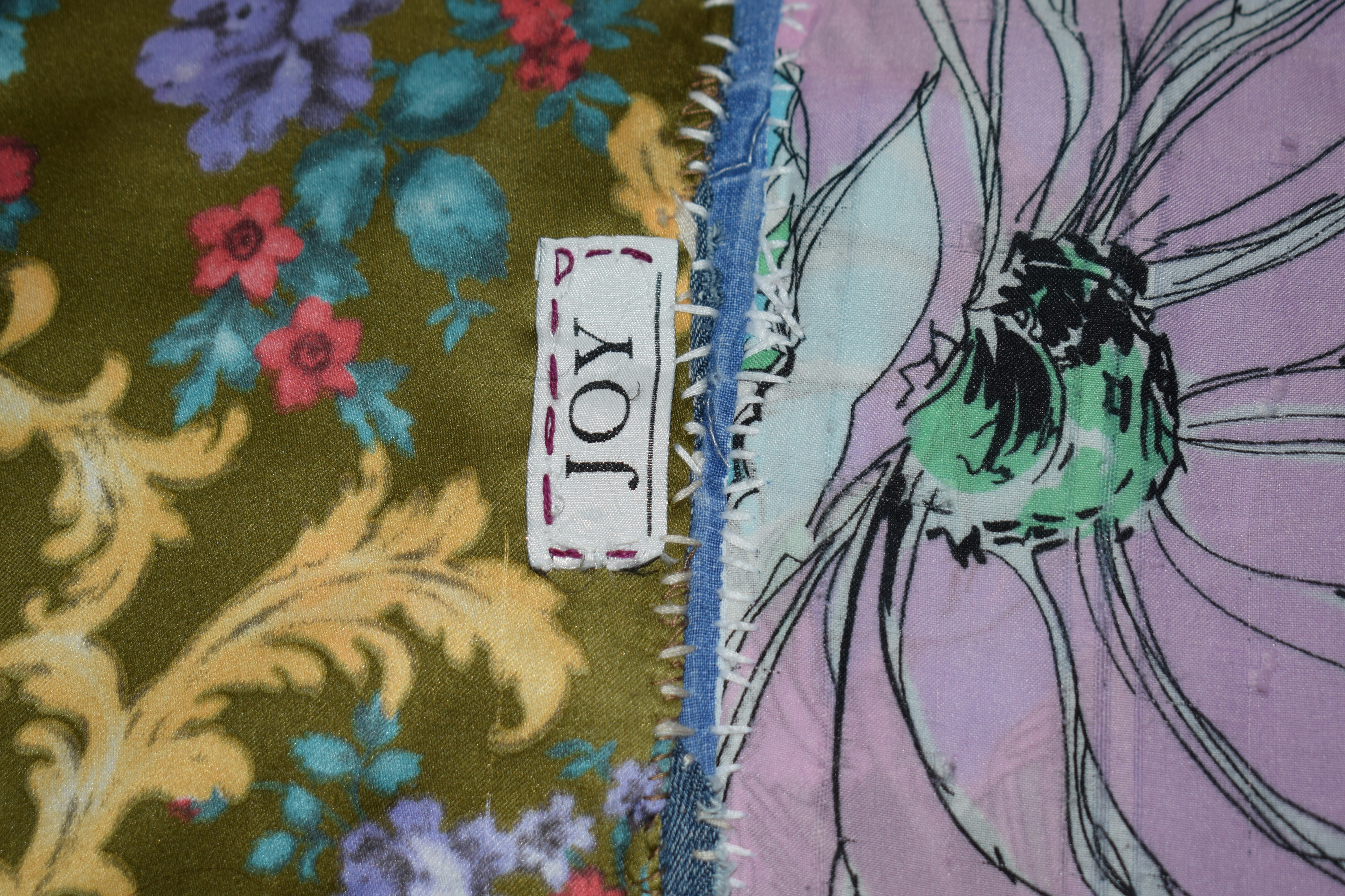 A fabric label reading JOY stitched onto a patchwork of floral and patterned textiles