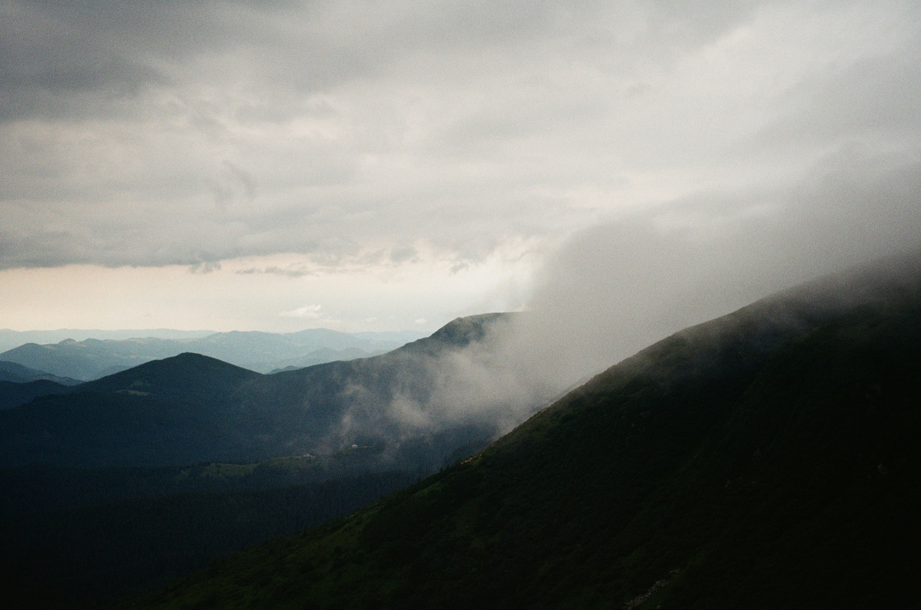 Clouds rolling over dark mountain ridges under a heavy overcast sky
