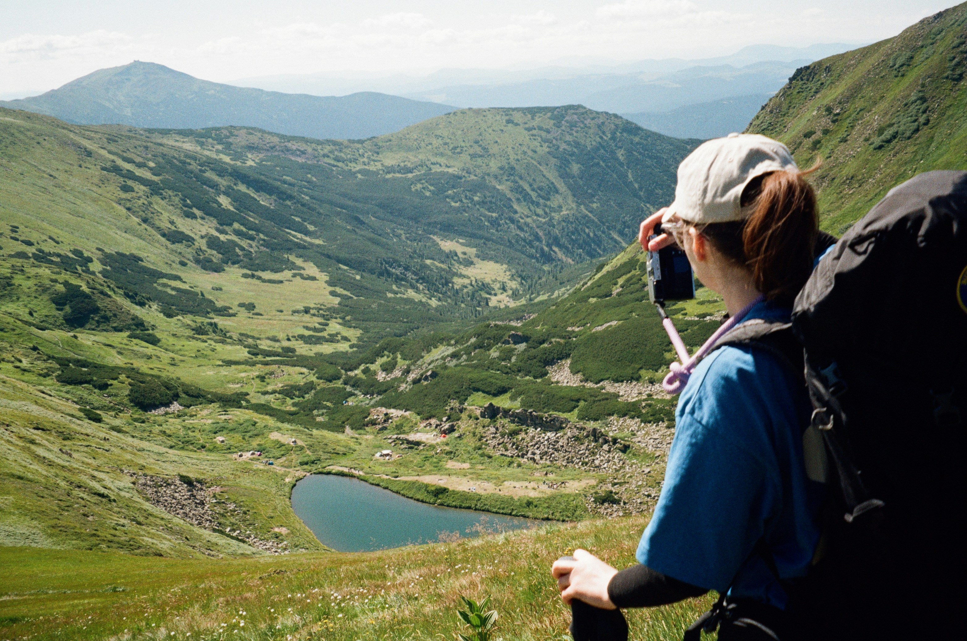 A person with a backpack photographing a mountain valley with a small lake