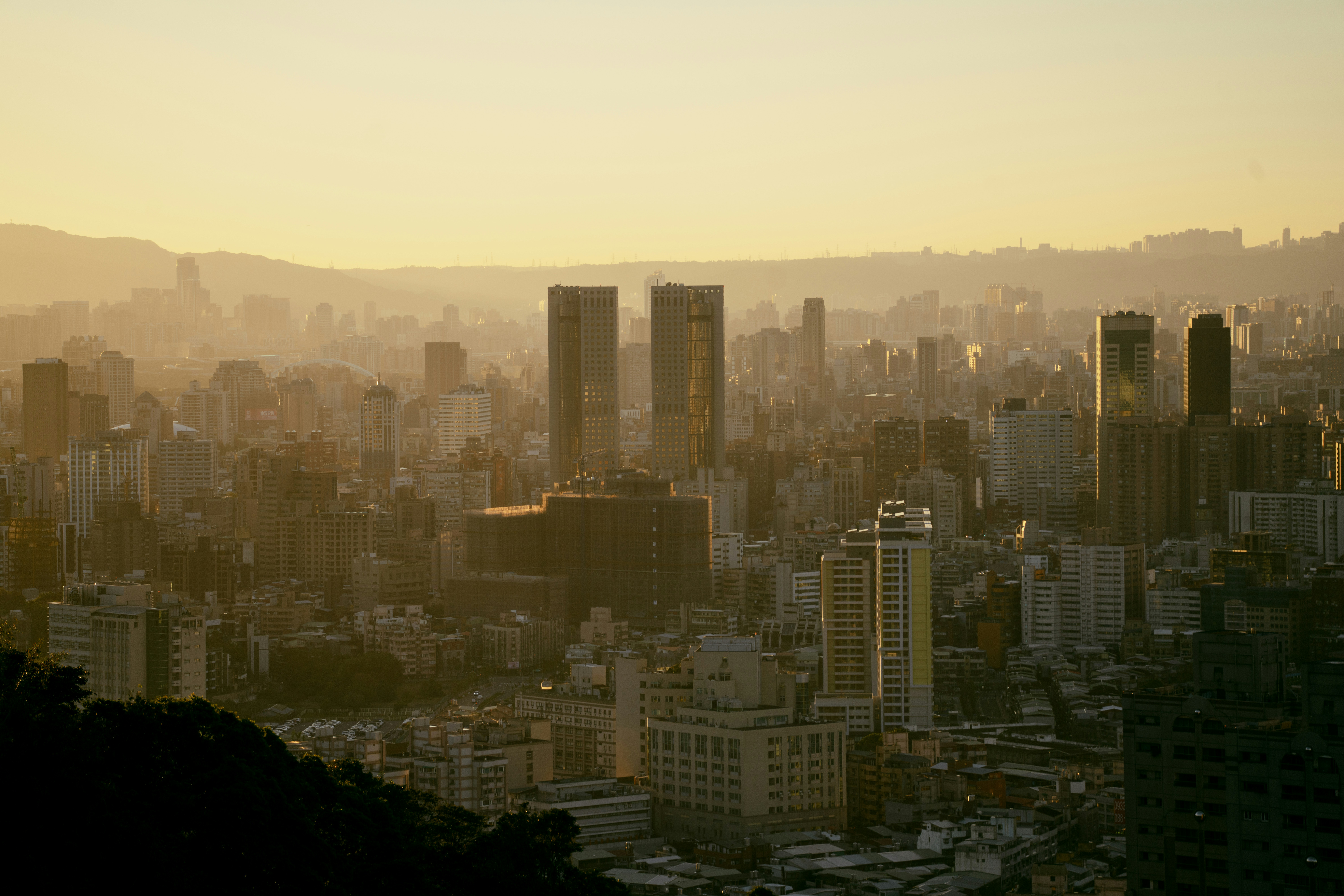 A dense cityscape under a warm golden sky with long shadows and distant mountains