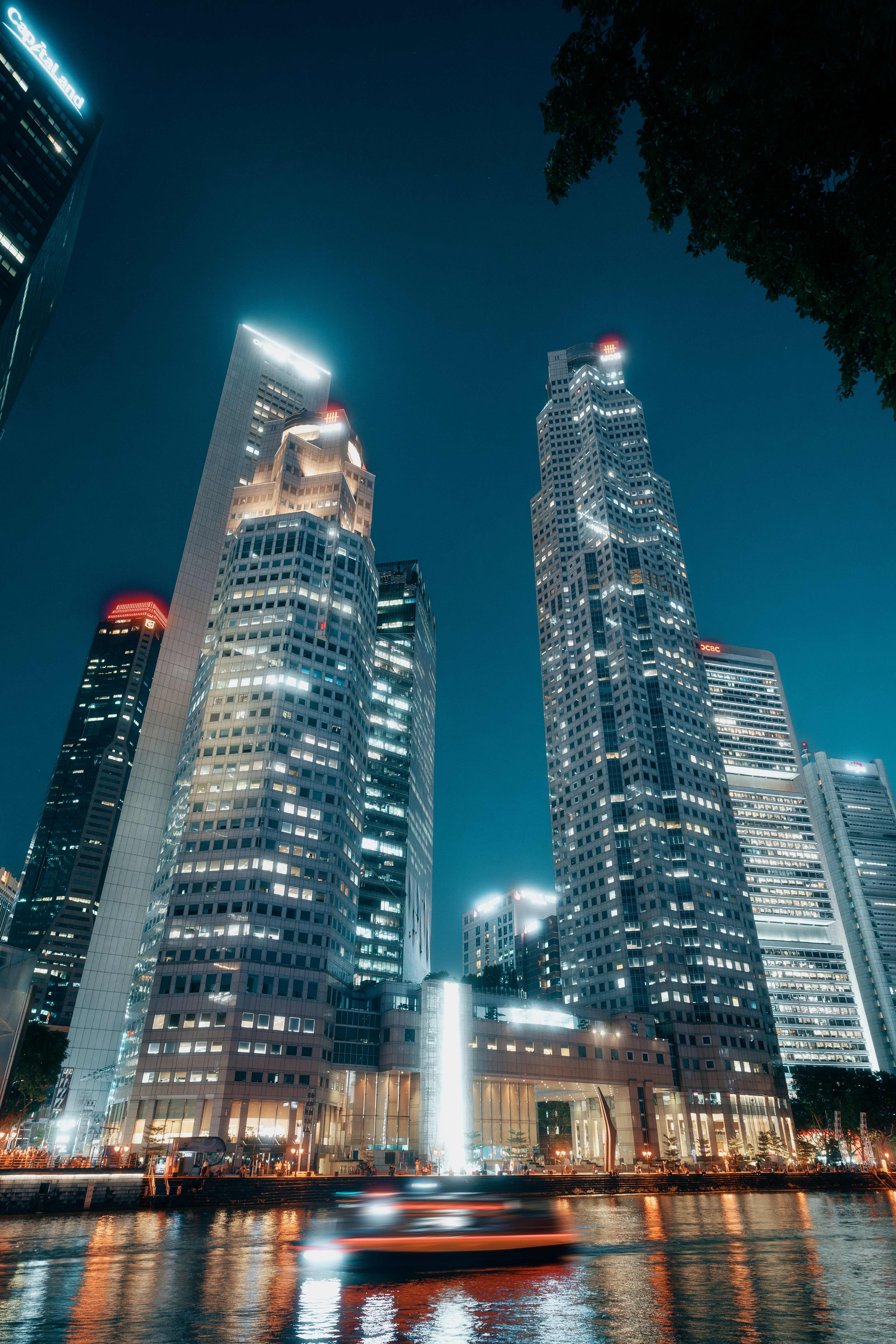 Illuminated skyscrapers at night along the Singapore River with a blurred boat in the foreground