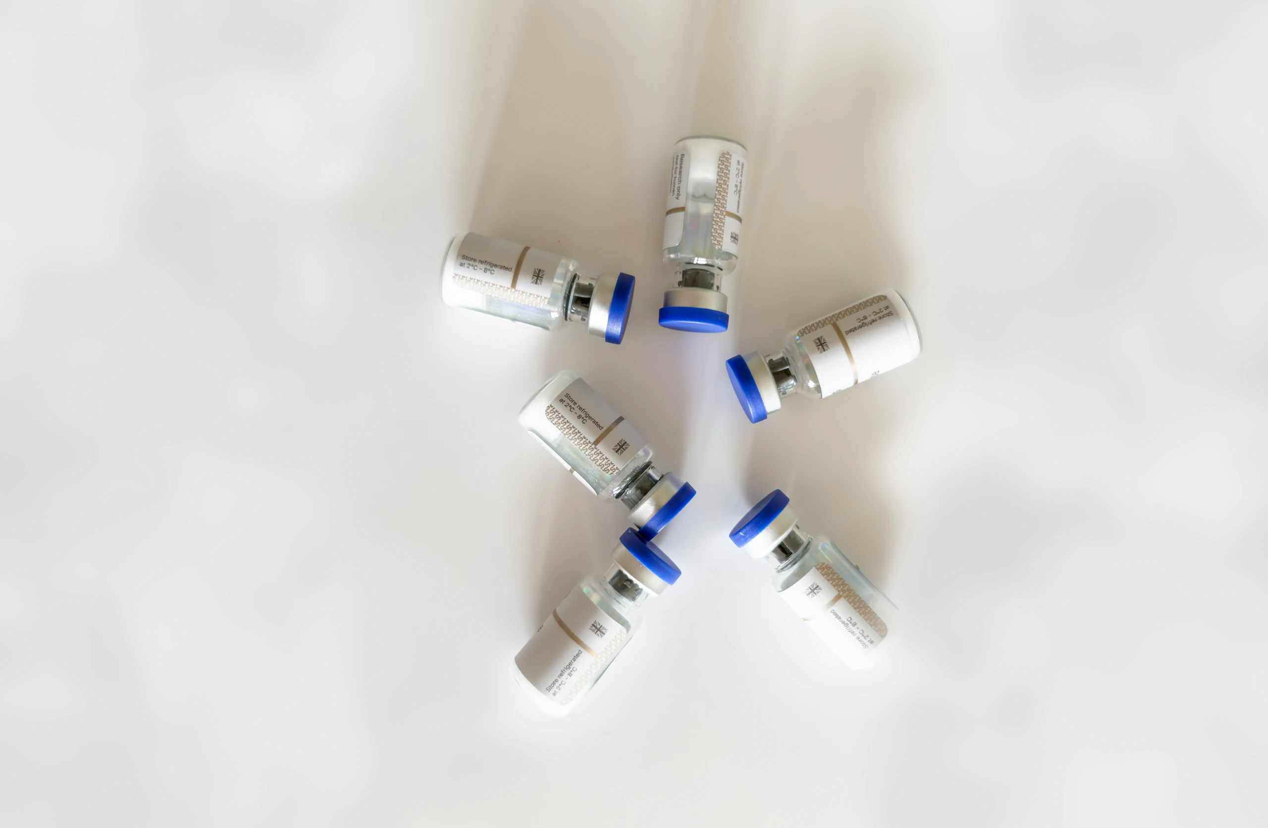Five small glass medicine vials with blue caps arranged in a circle on a white surface.