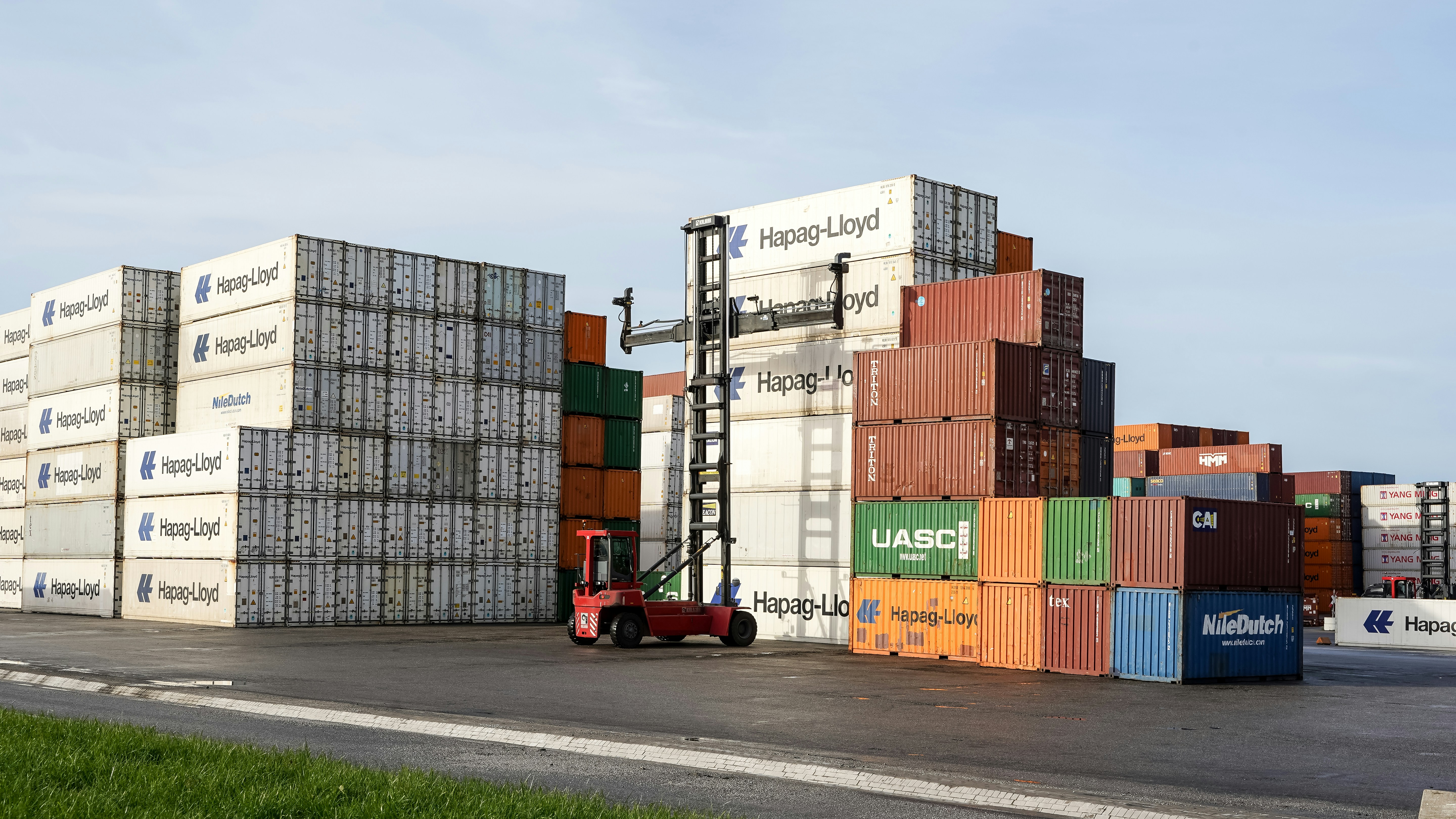 A red reach stacker parked beside tall stacks of colorful shipping containers in a port