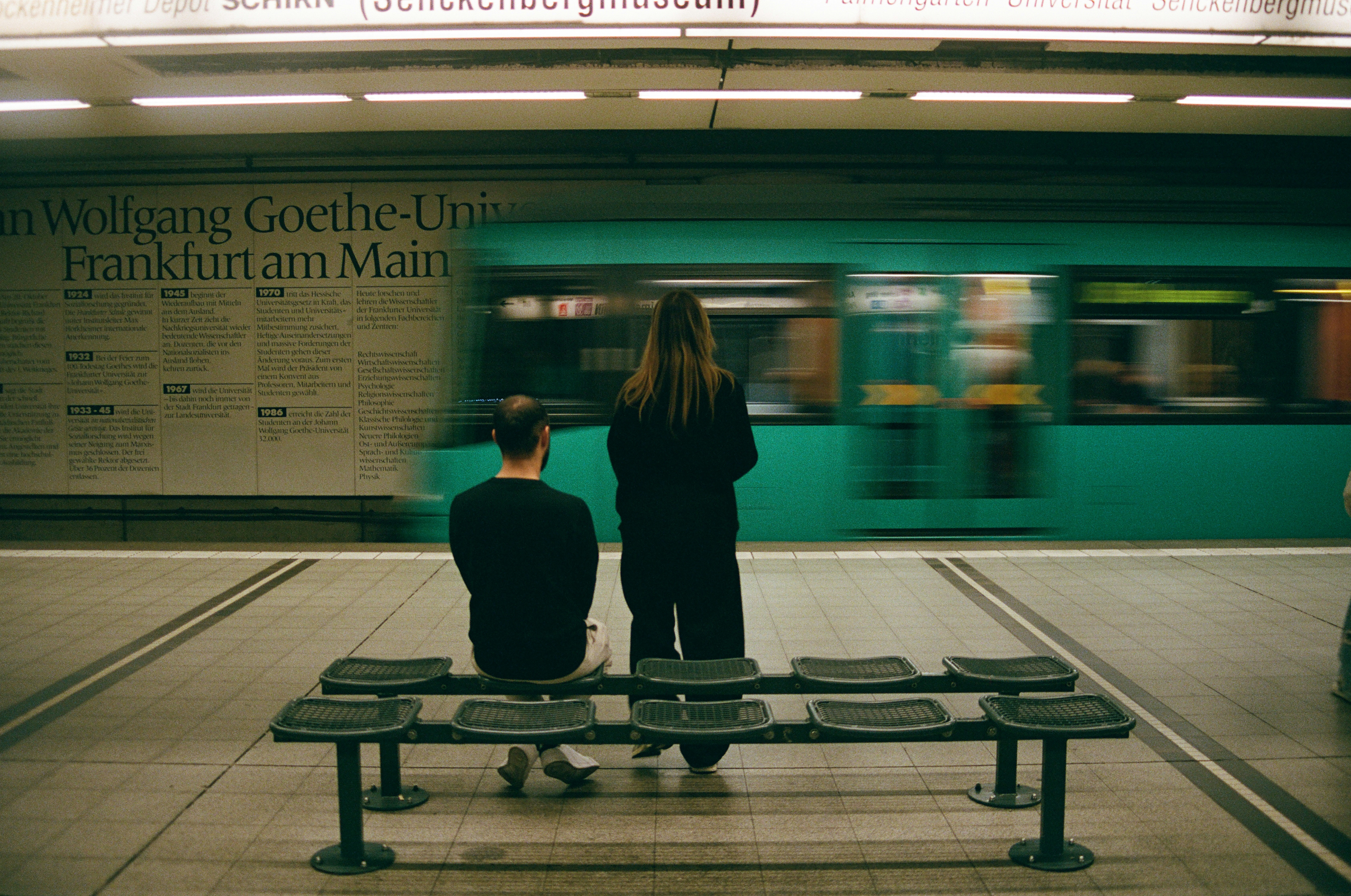 Two people on a bench at a subway station in Frankfurt as a train passes