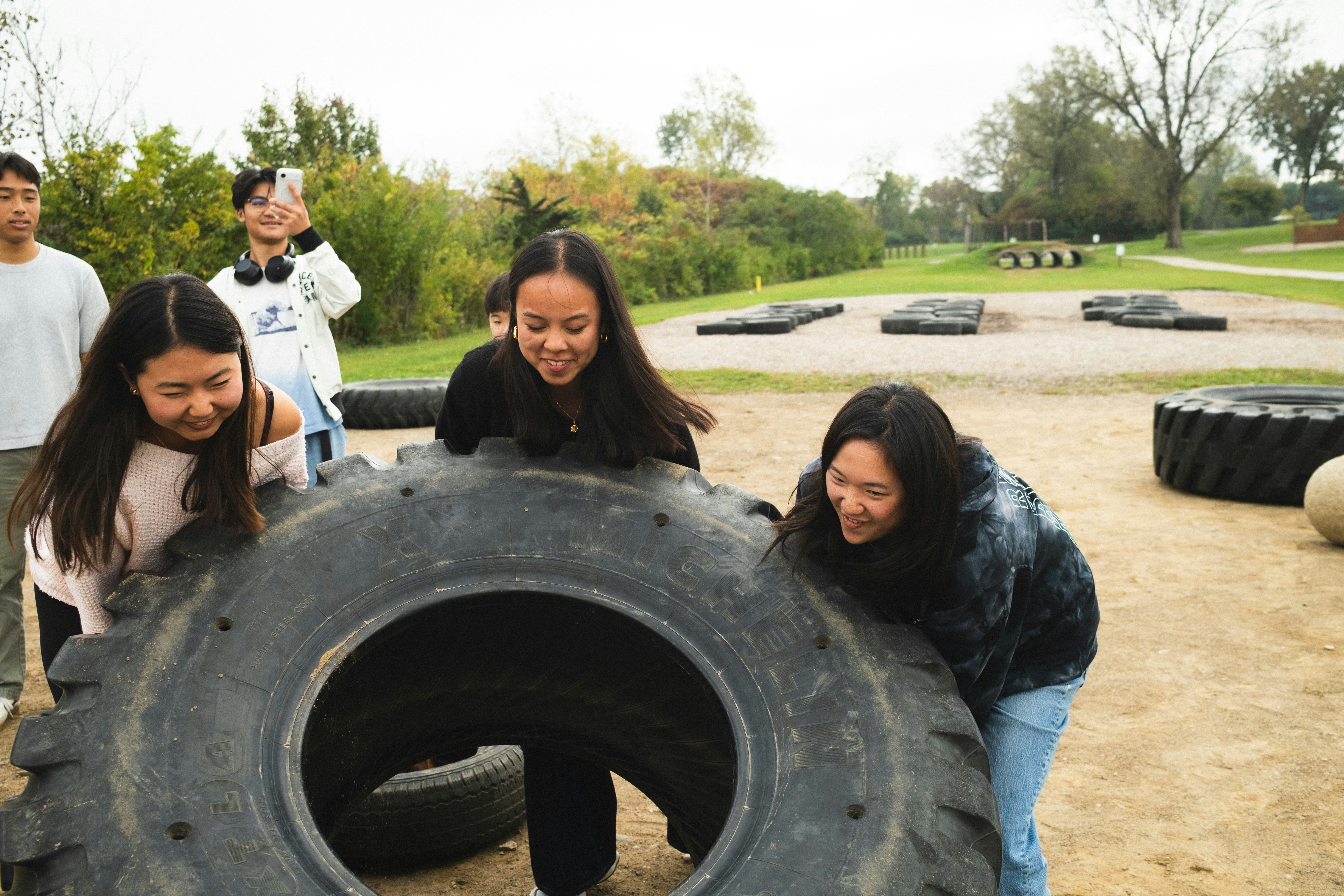 A group of young adults pushing a large tractor tire on a dirt field