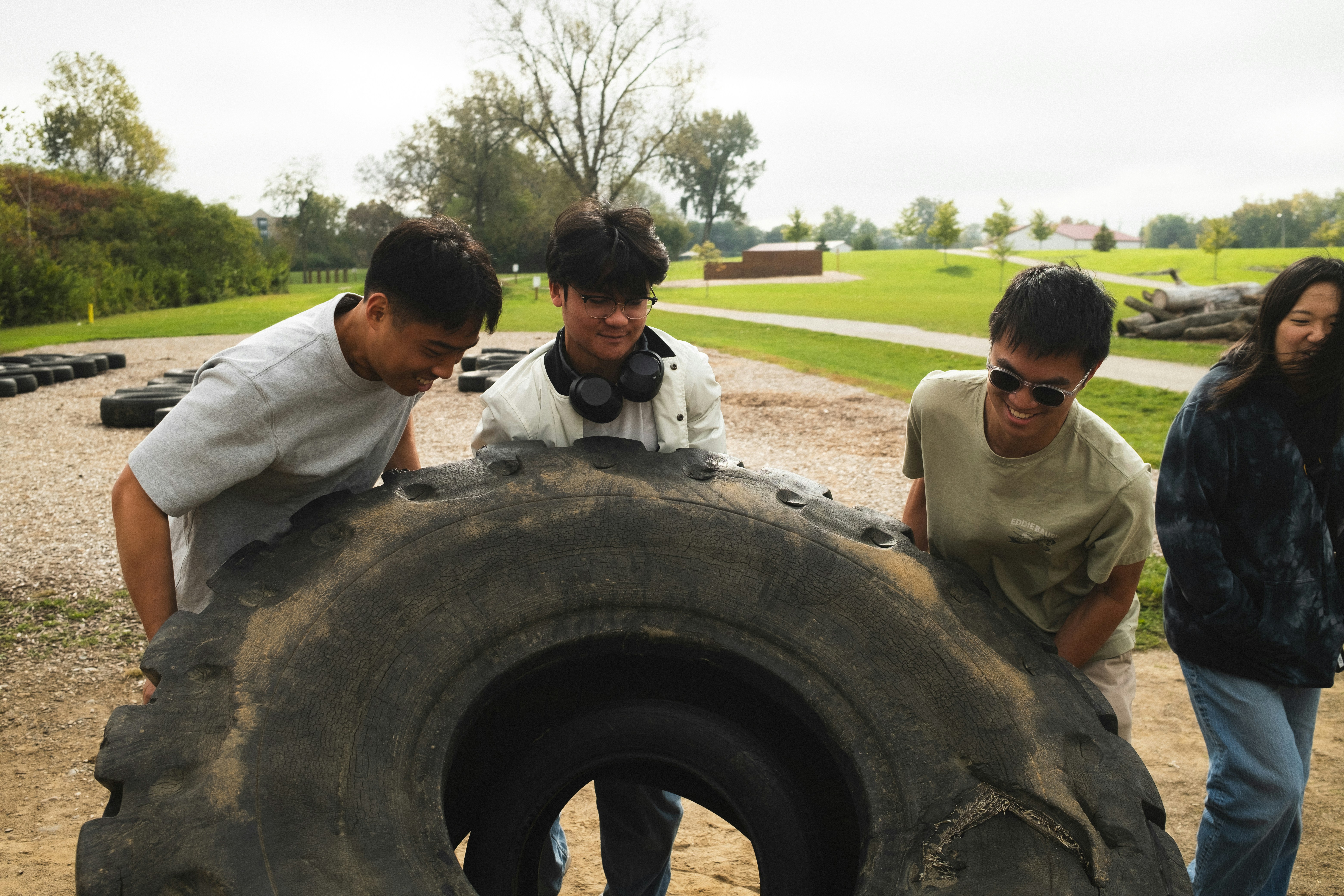 Three young adults pushing a large tractor tire in a park