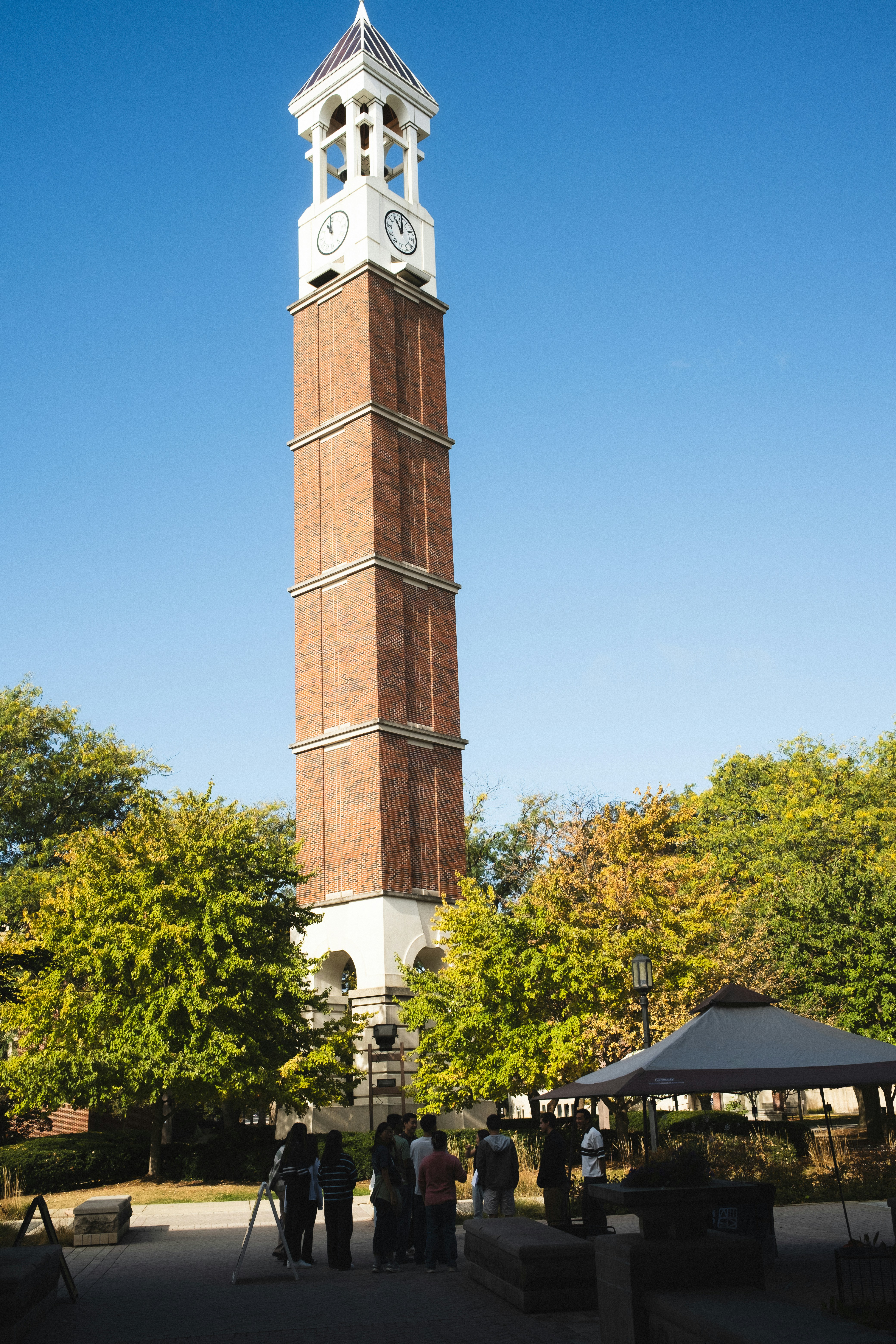 A group of people standing near a tall brick clock tower on a sunny day