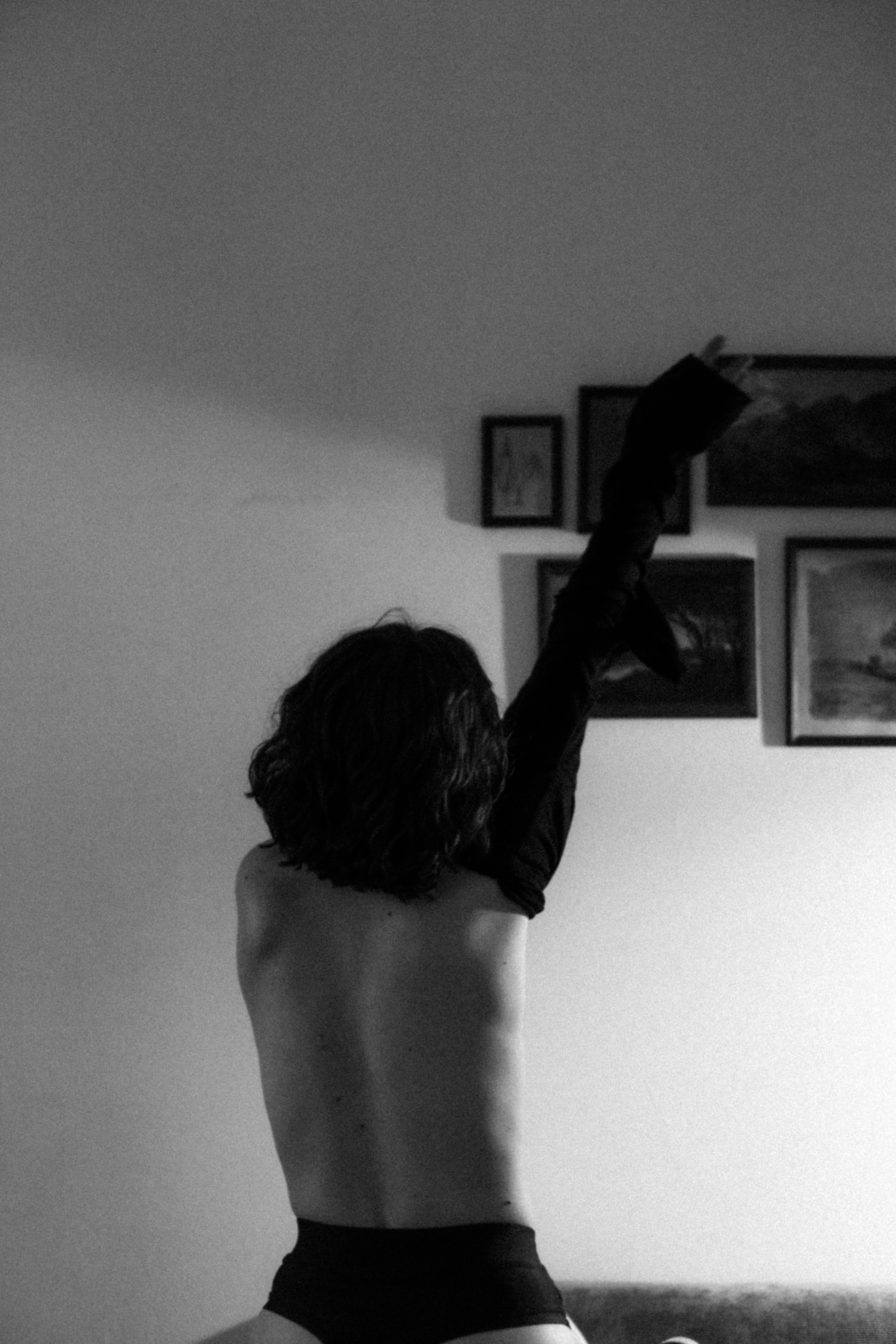 A person from behind removing a black shirt in a room with framed pictures
