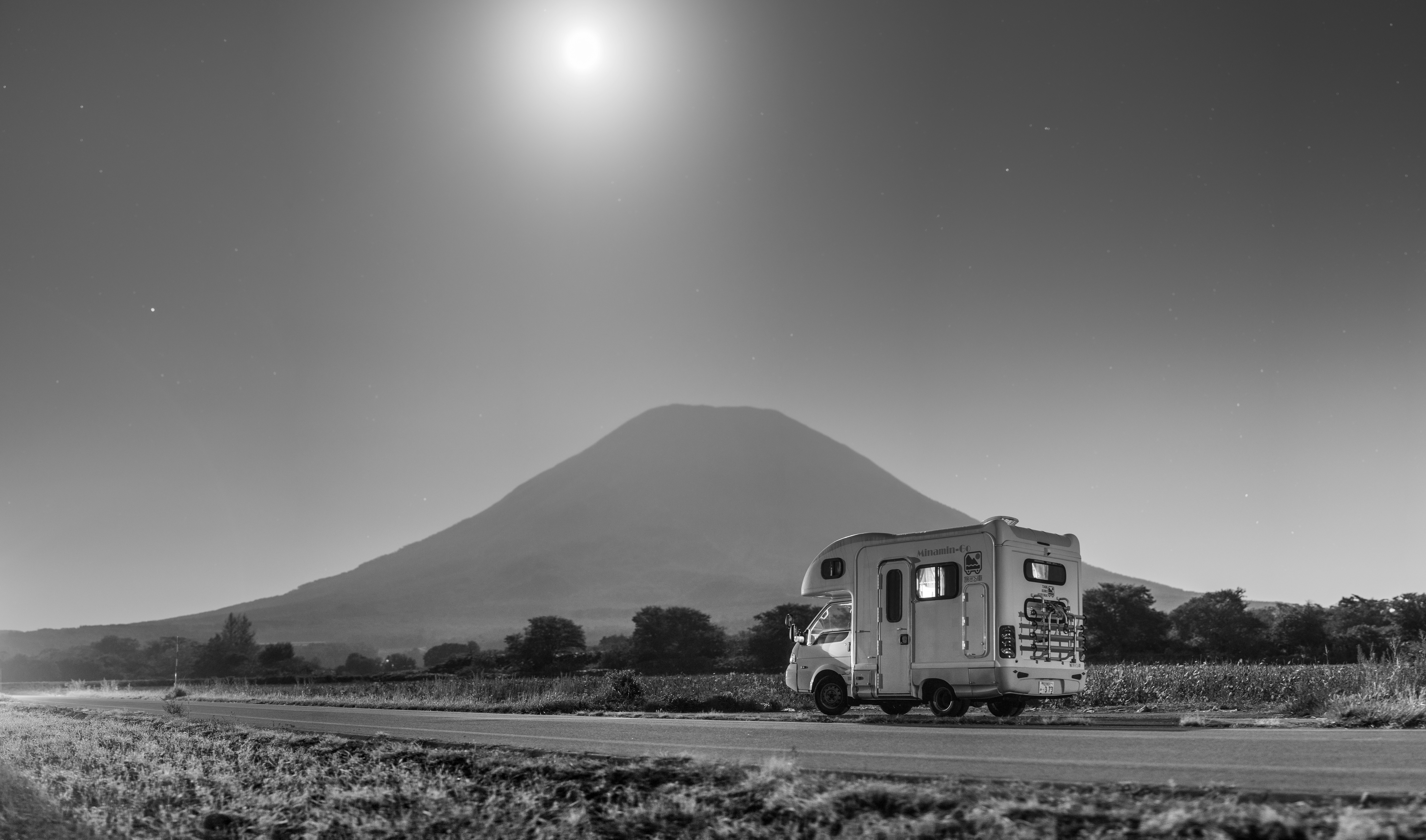 A camper van parked on a roadside beneath a large mountain under a bright moon