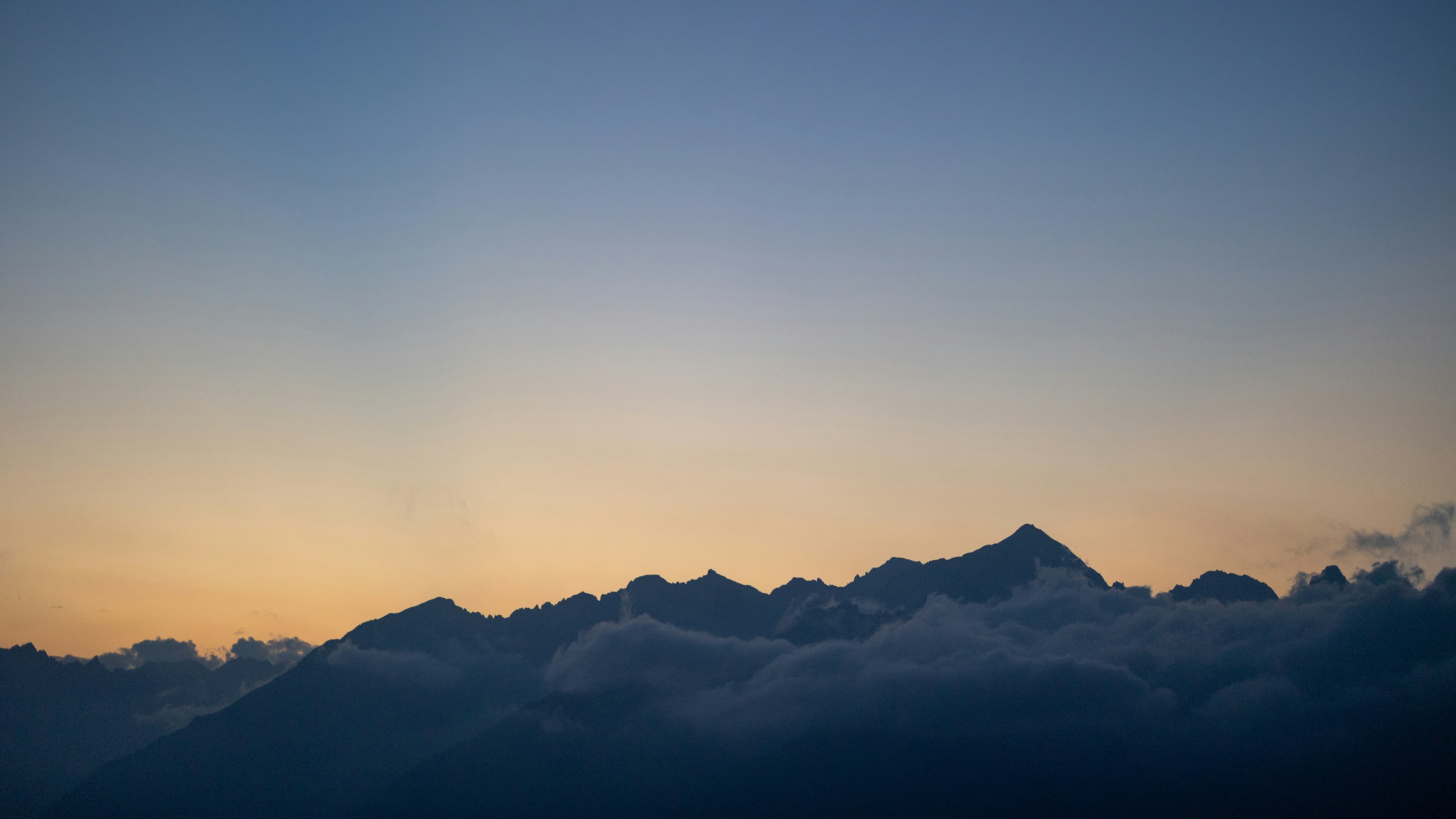Mountain silhouettes against a warm orange and blue sky with low clouds