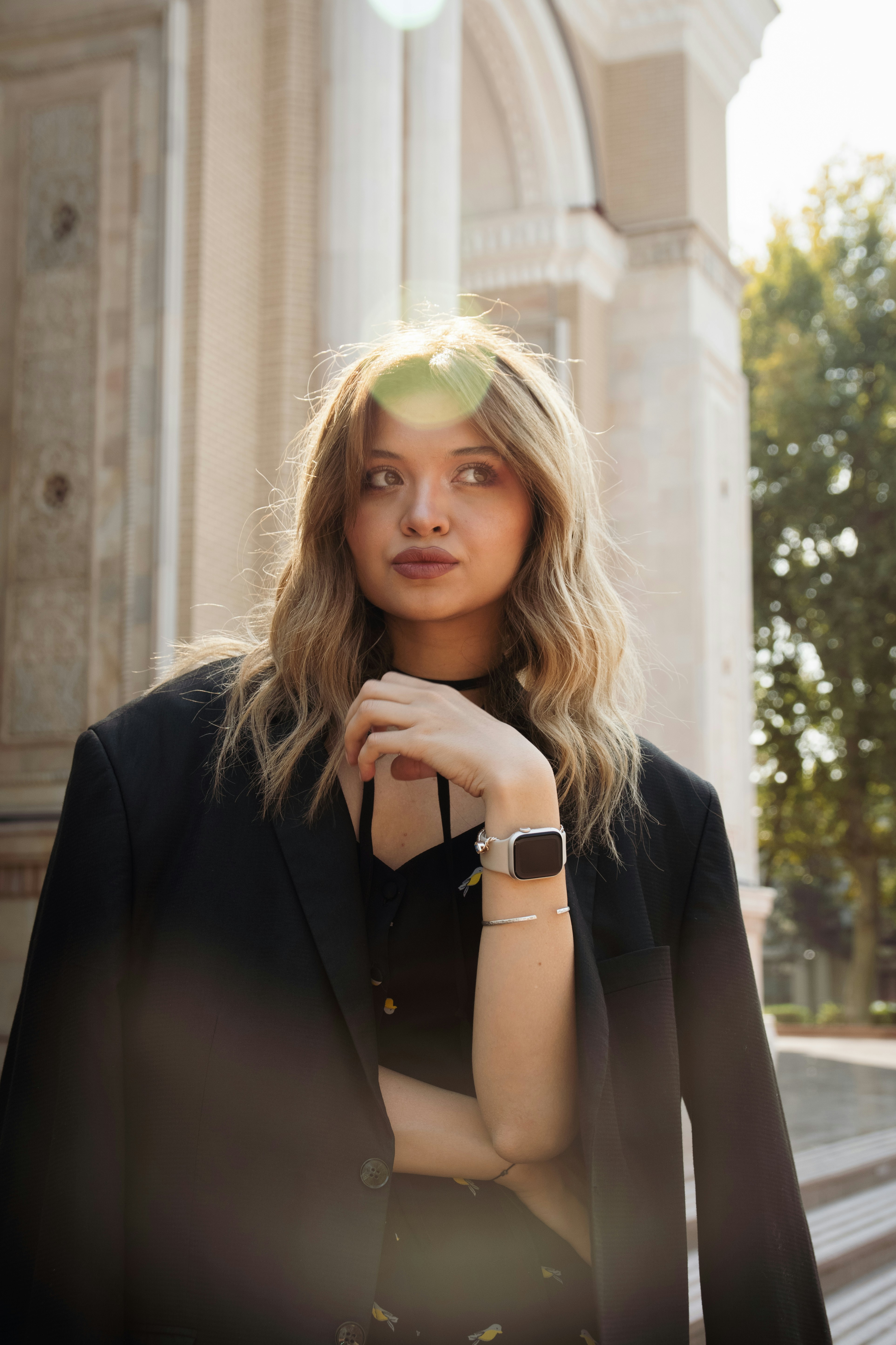 A woman in a black blazer and smartwatch standing outdoors in warm sunlight
