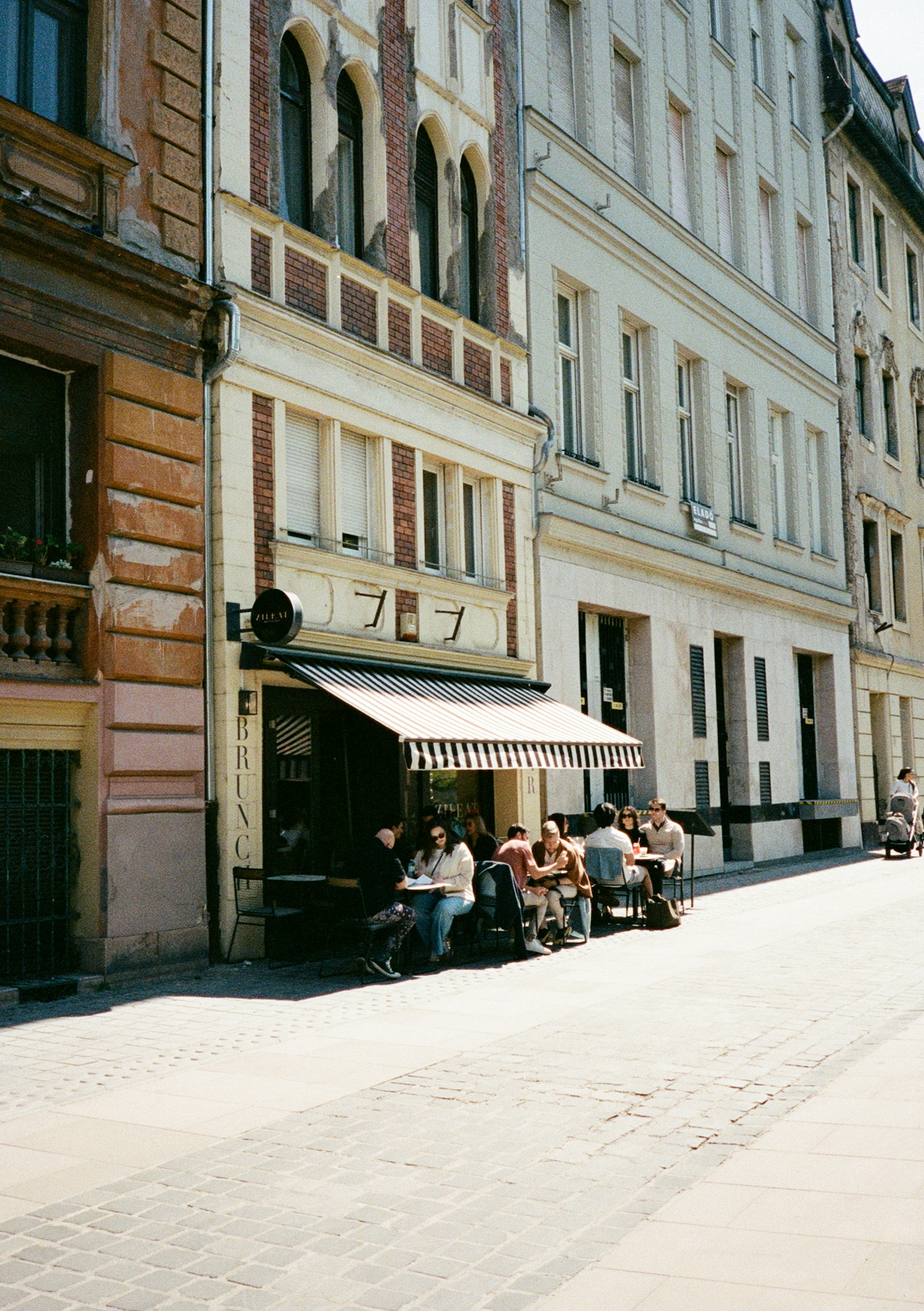 Menschen, die an Tischen unter einem gestreiften Vordach vor einem Café in Budapest sitzen