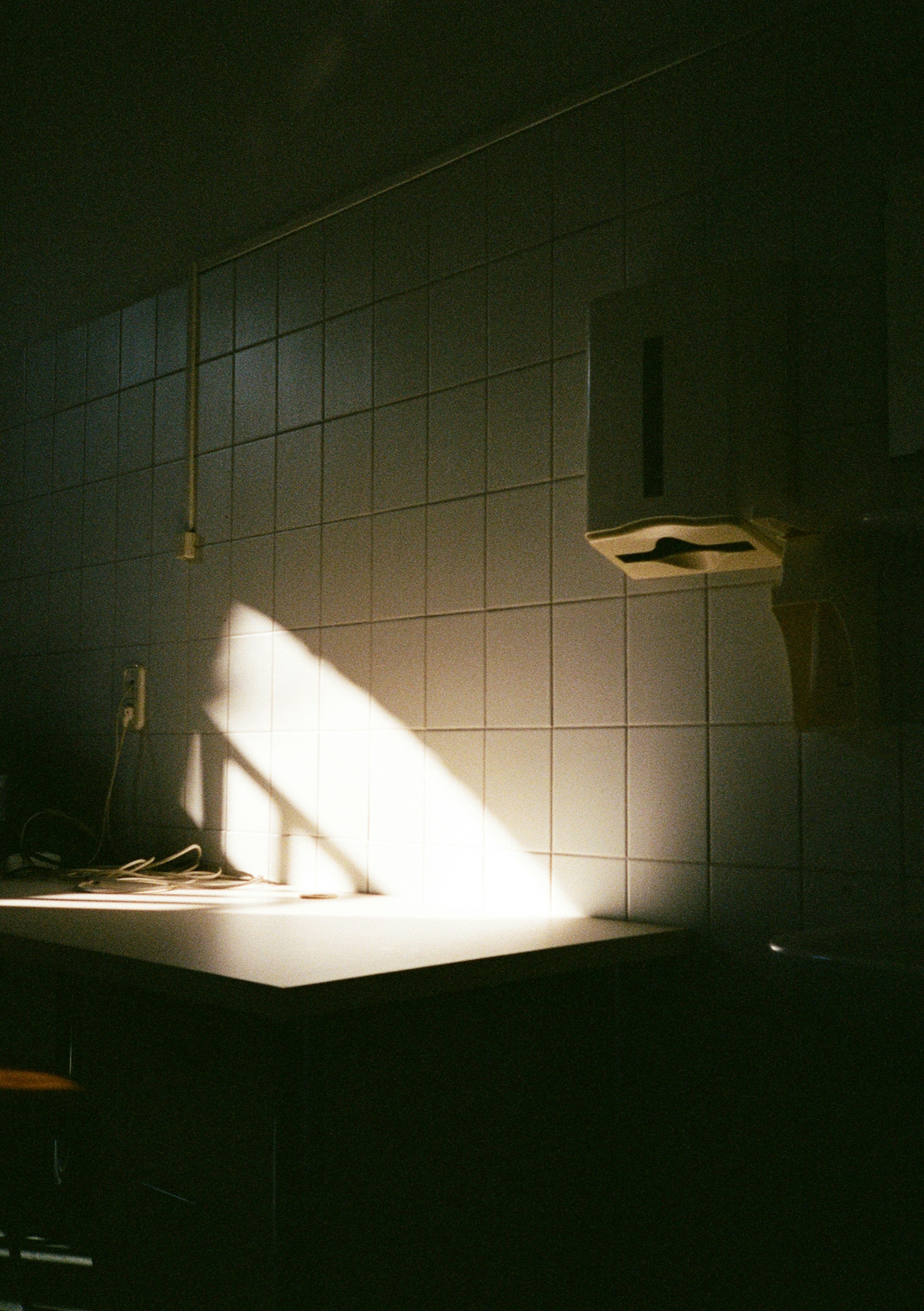 Ein heller Lichtstrahl trifft eine geflieste Wand über einem Tisch in einem dunklen Raum