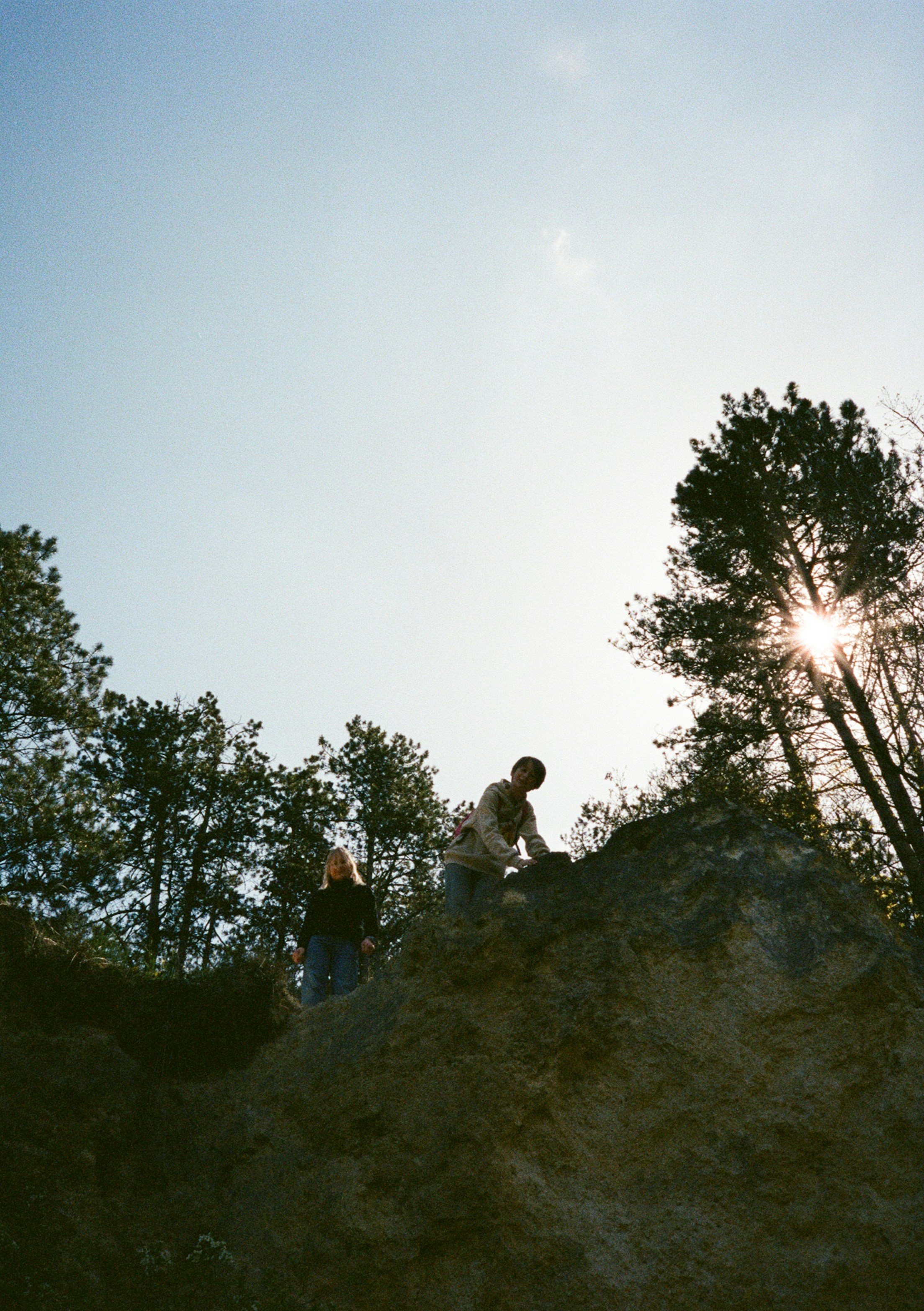 Two people on a rocky outcrop in Solymár with pine trees and low sun