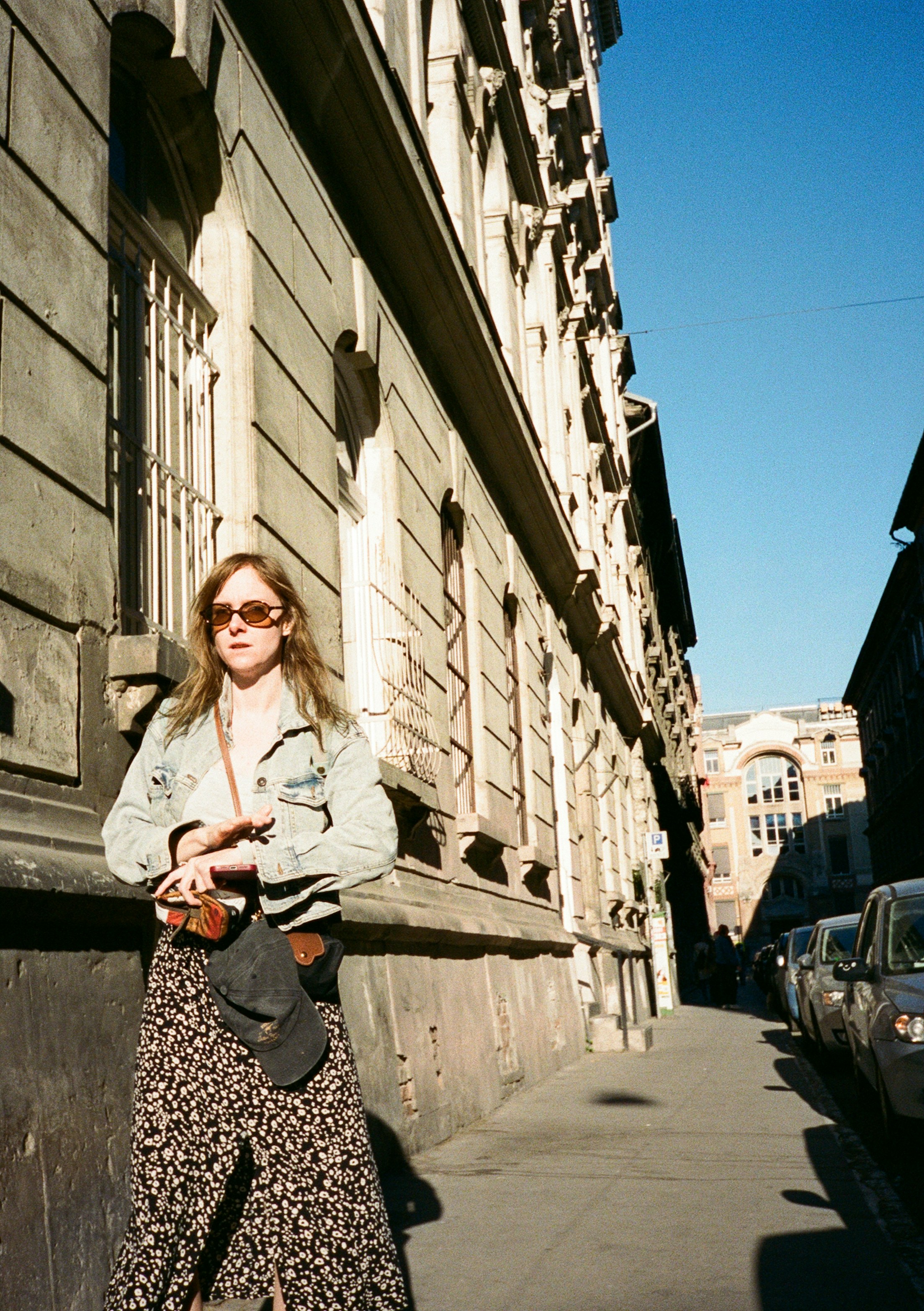 Eine Frau in Jeansjacke und gemustertem Rock auf einer sonnigen Straße in Budapest