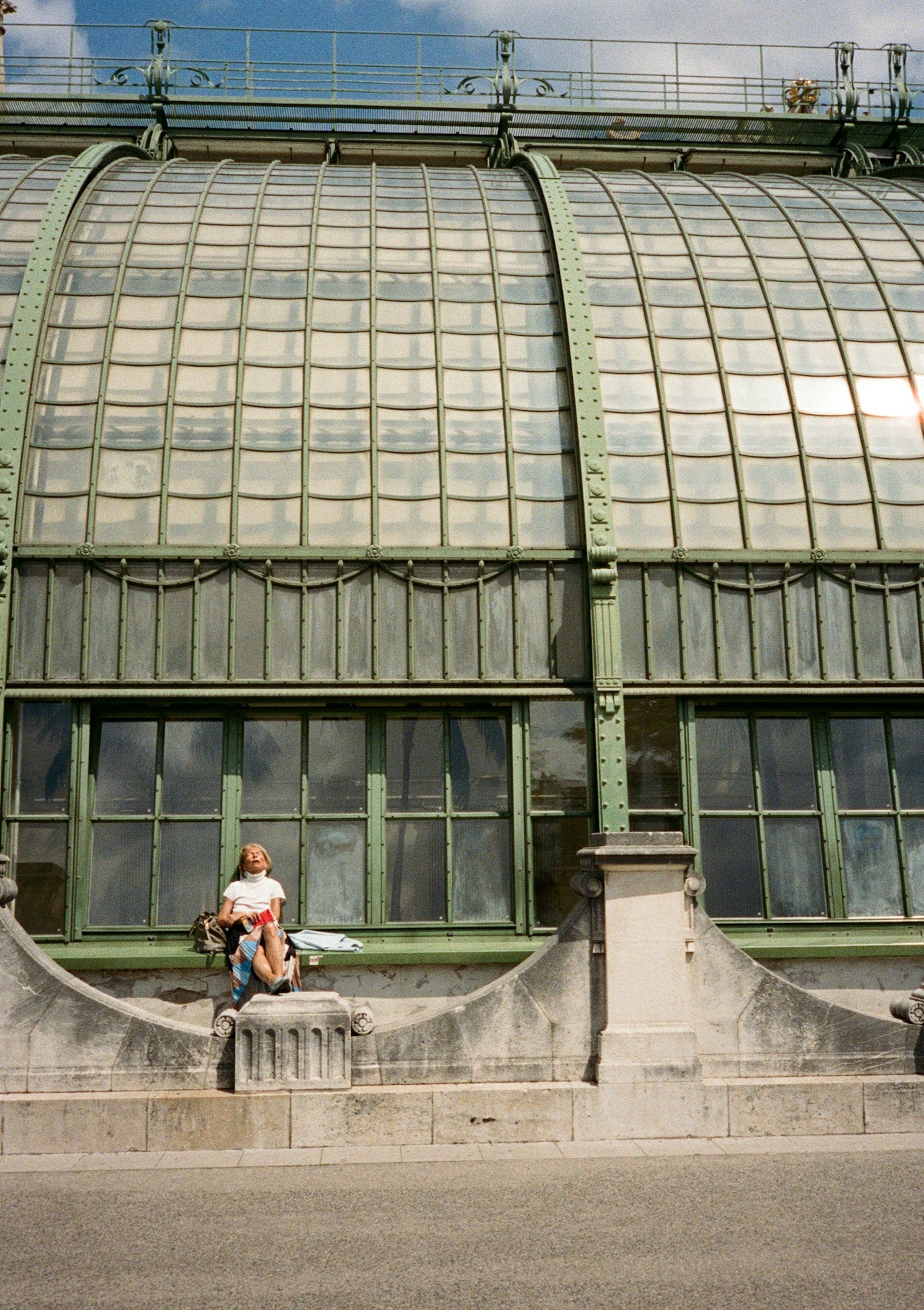 Ein Erwachsener, der auf einem Steinvorsprung vor dem gläsernen Palmenhaus in Wien sitzt